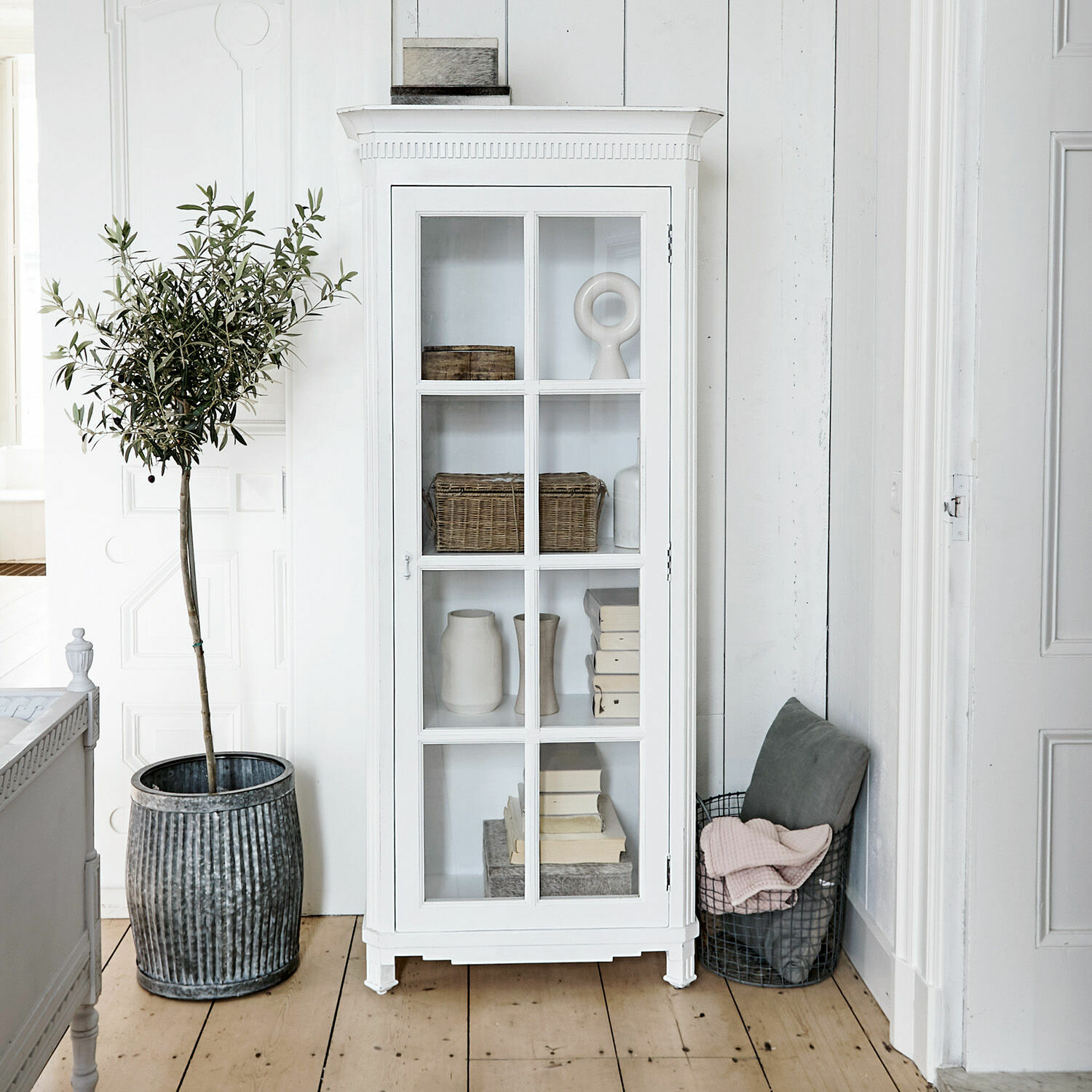 Weiße Holzvitrine mit Glastür und Vintage-Dekorationen in hellem Raum