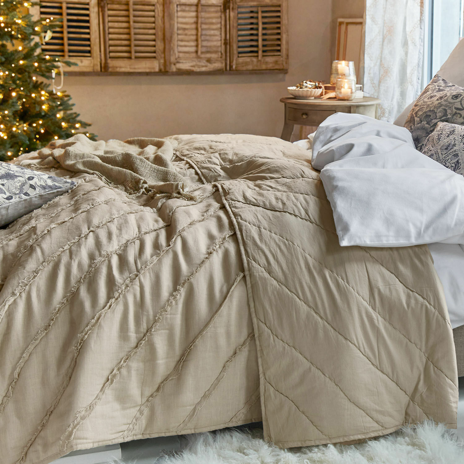 Beige Bettdecke aus weichem Material in gemütlichem Raum mit Weihnachtsbaum und Kerzen