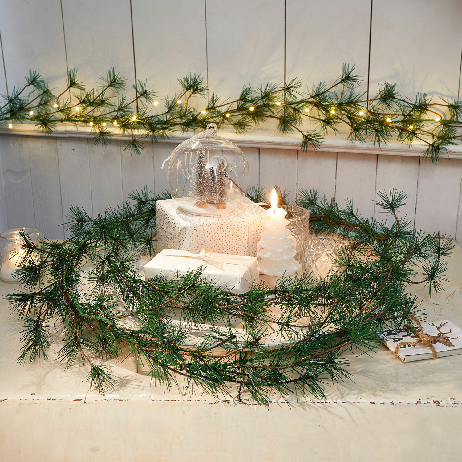 Dekorativer Kranz aus grünen Kiefernzweigen mit weißen Kerzen und Weihnachtsdeko auf Tisch