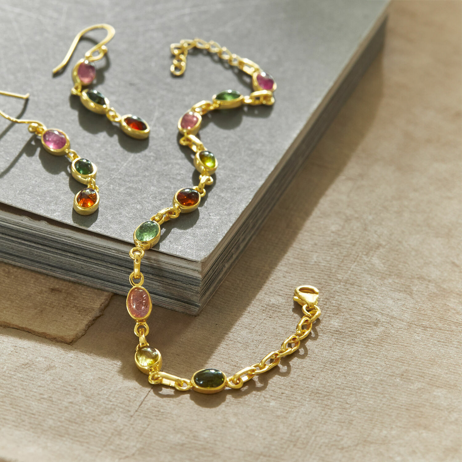 Goldenes Armband und Ohrringe mit bunten Steinen auf grauem Hintergrund, Damenschmuck