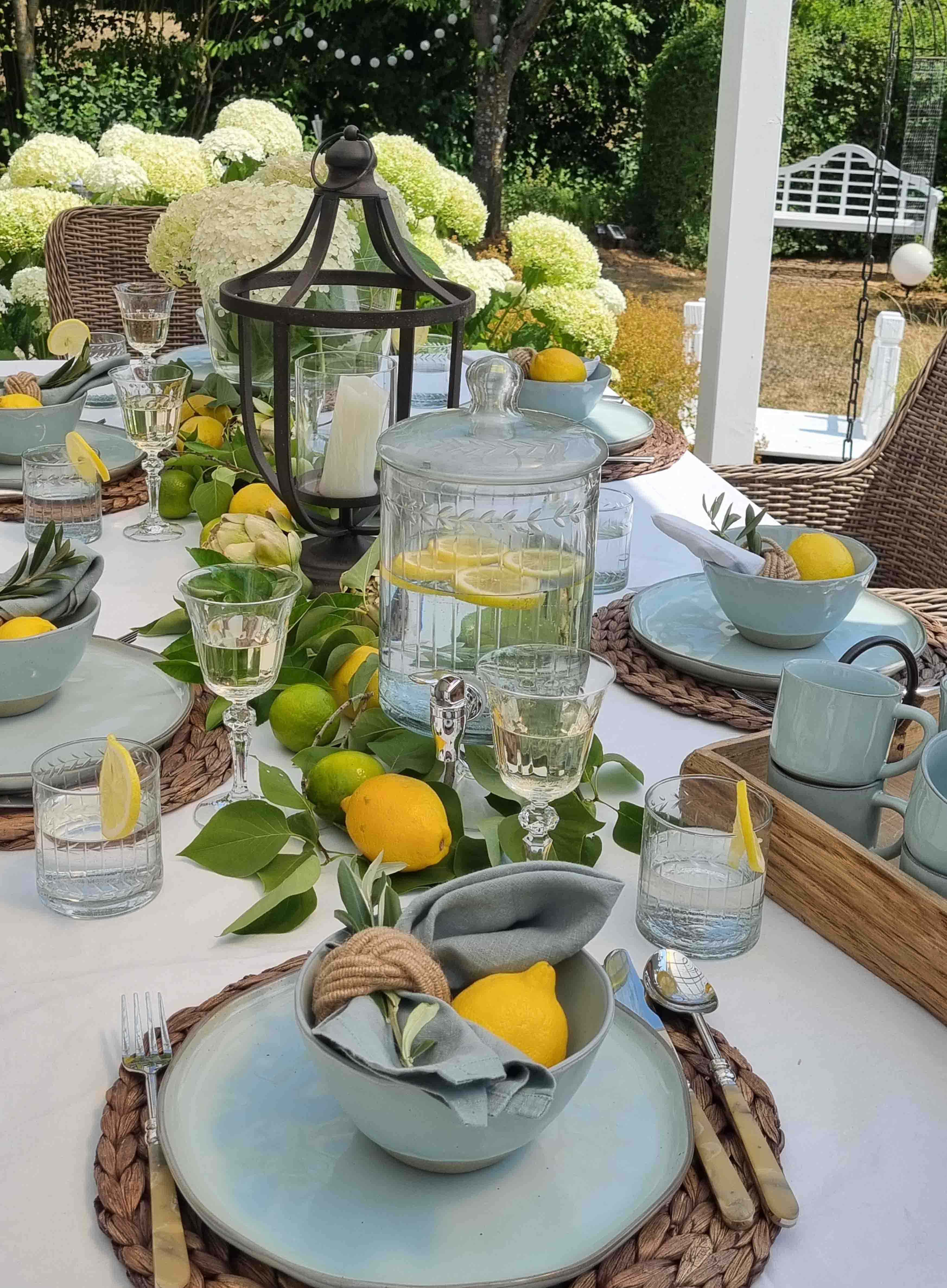 Sommerlicher Gartentisch mit blauer Keramik, Zitronen und Laterne vor weißen Hortensien