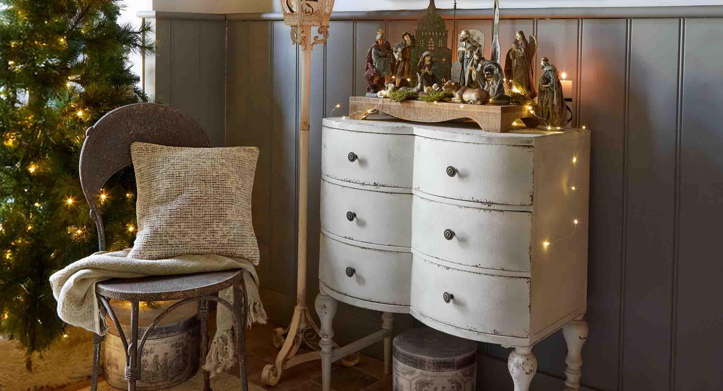 Weisse, antik wirkende Kommode mit hölzerner Weihnachtskrippe und festlicher Dekoration in gemütlichem Raum