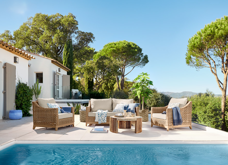 Beiges Rattan-Gartenmöbel-Set am Pool auf Terrasse mit Blick auf Bäume und blauen Himmel