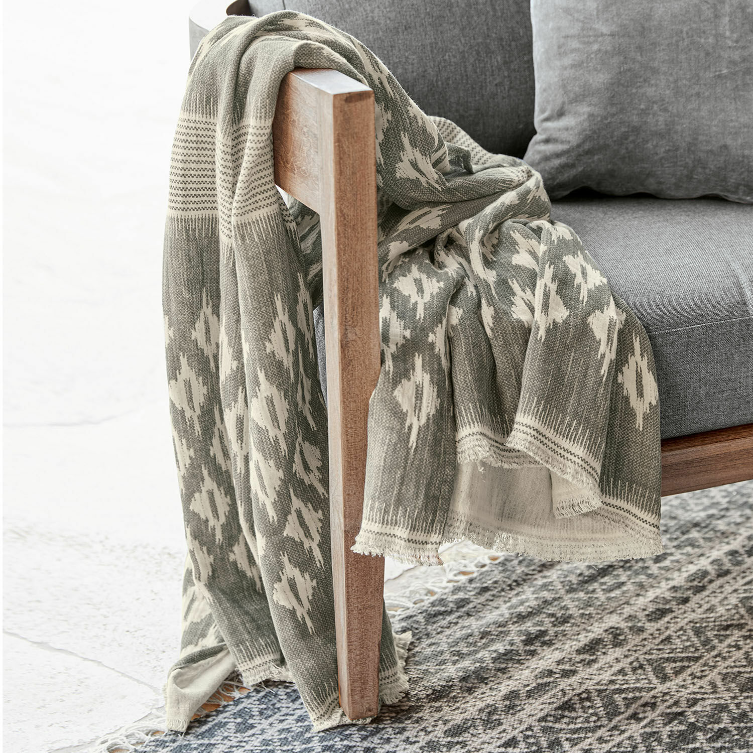 Grauer Baumwollplaid mit geometrischem Muster auf Holzstuhl und Teppich, Wohnaccessoire