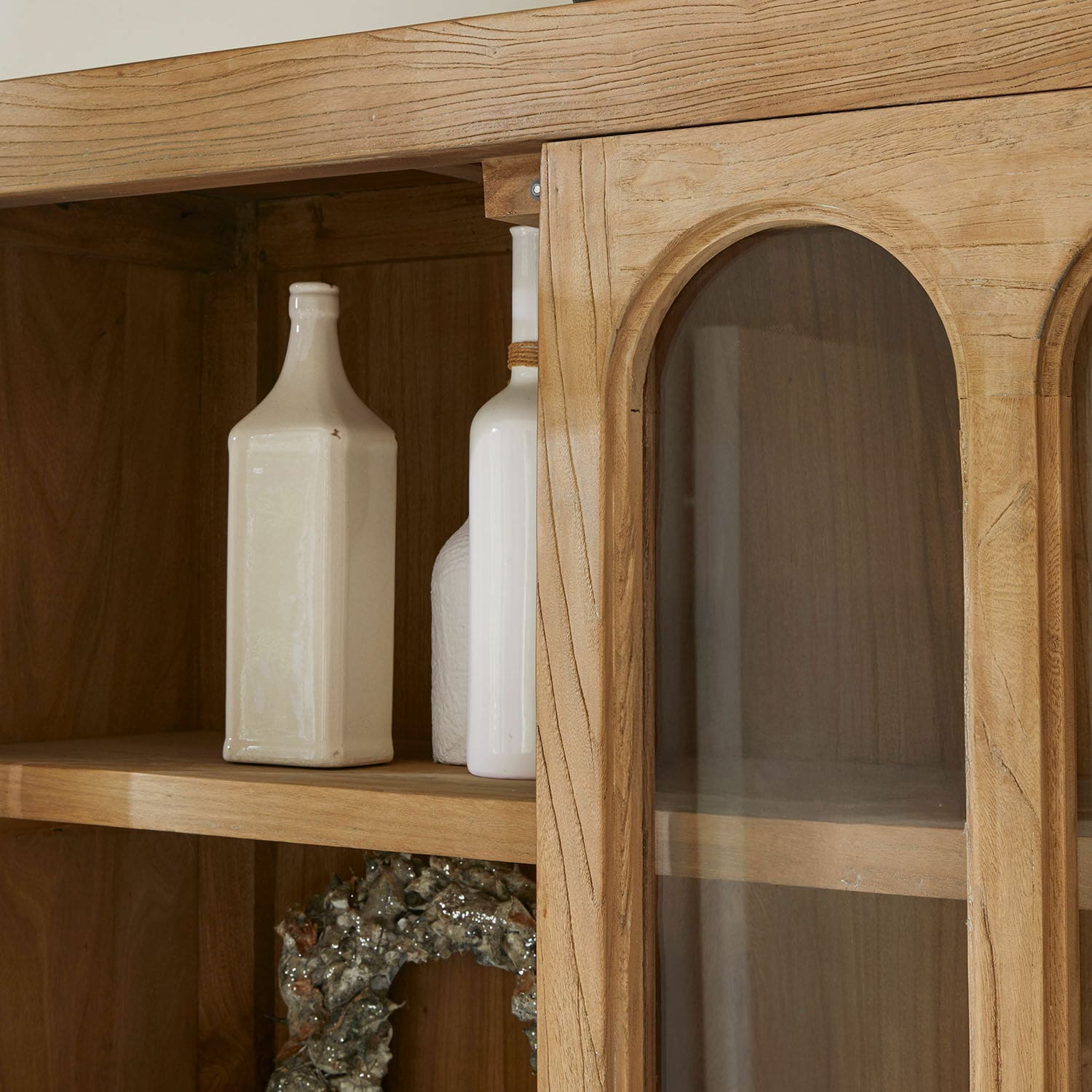 Holzschrank mit Glastür und dekorativen weißen Flaschen auf dem Regal