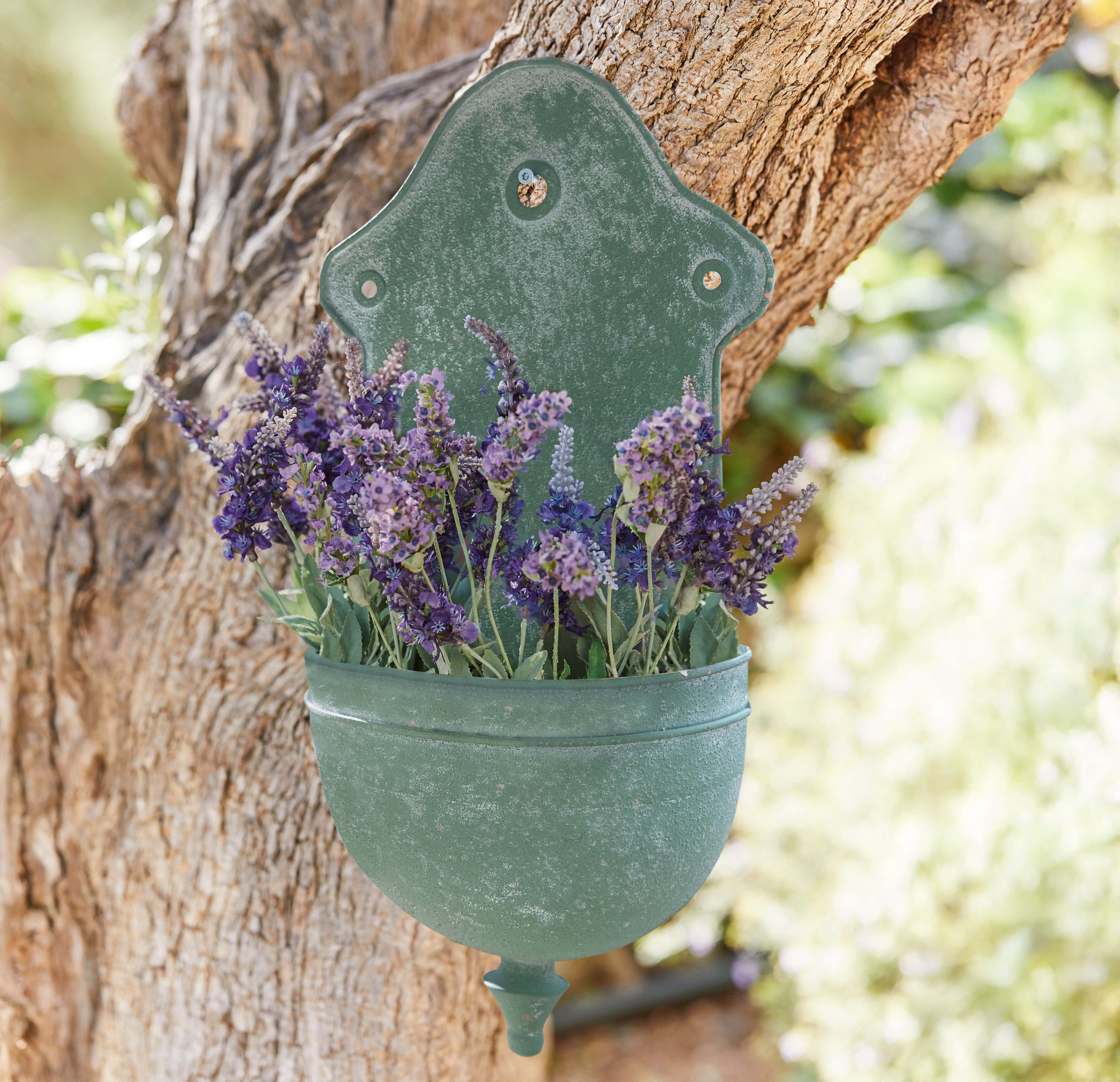 Grüne Metall-Wandblumenvase mit violetten Lavendelblüten an Baumstamm, Gartendekoration