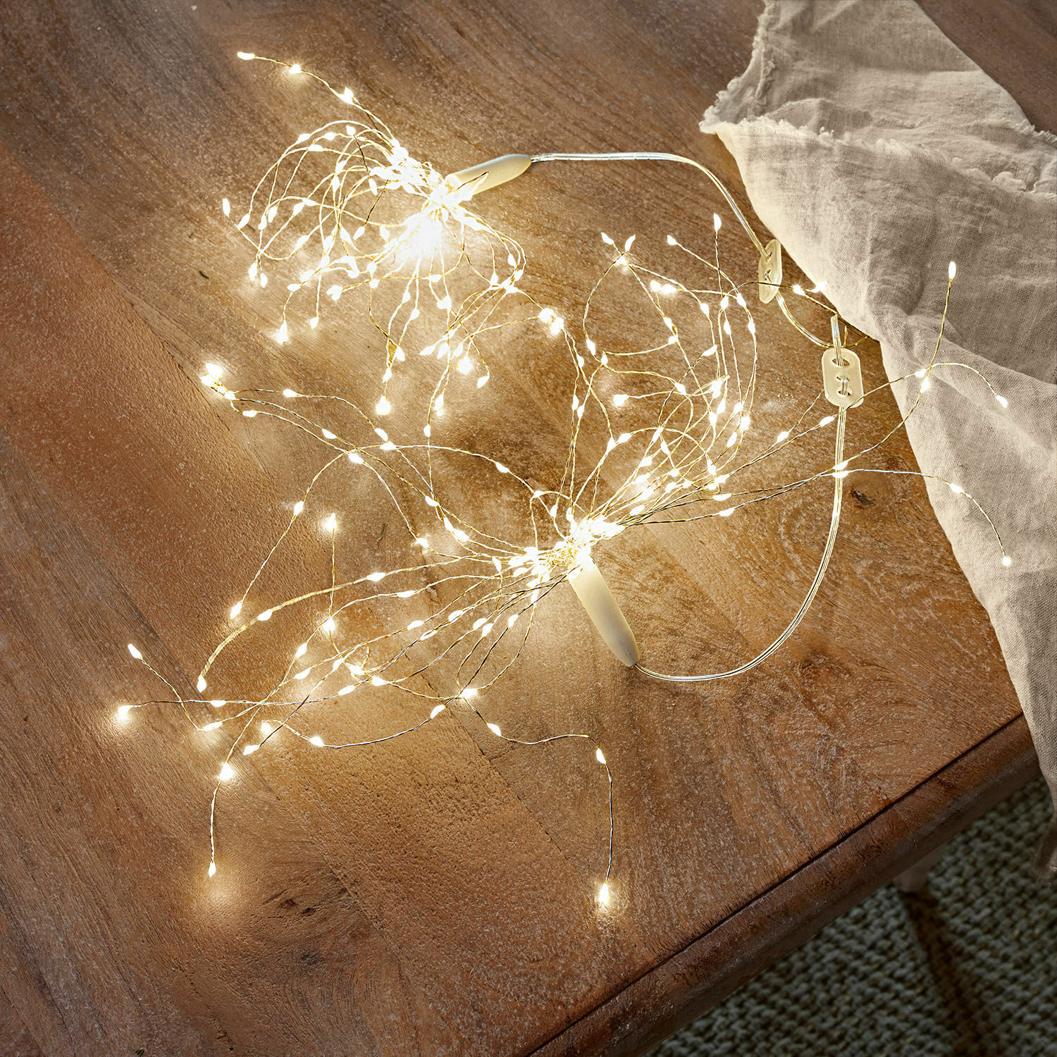 Feine LED-Lichterkette mit warmweißen Lichtern auf dünnen Drähten auf Holztisch liegend