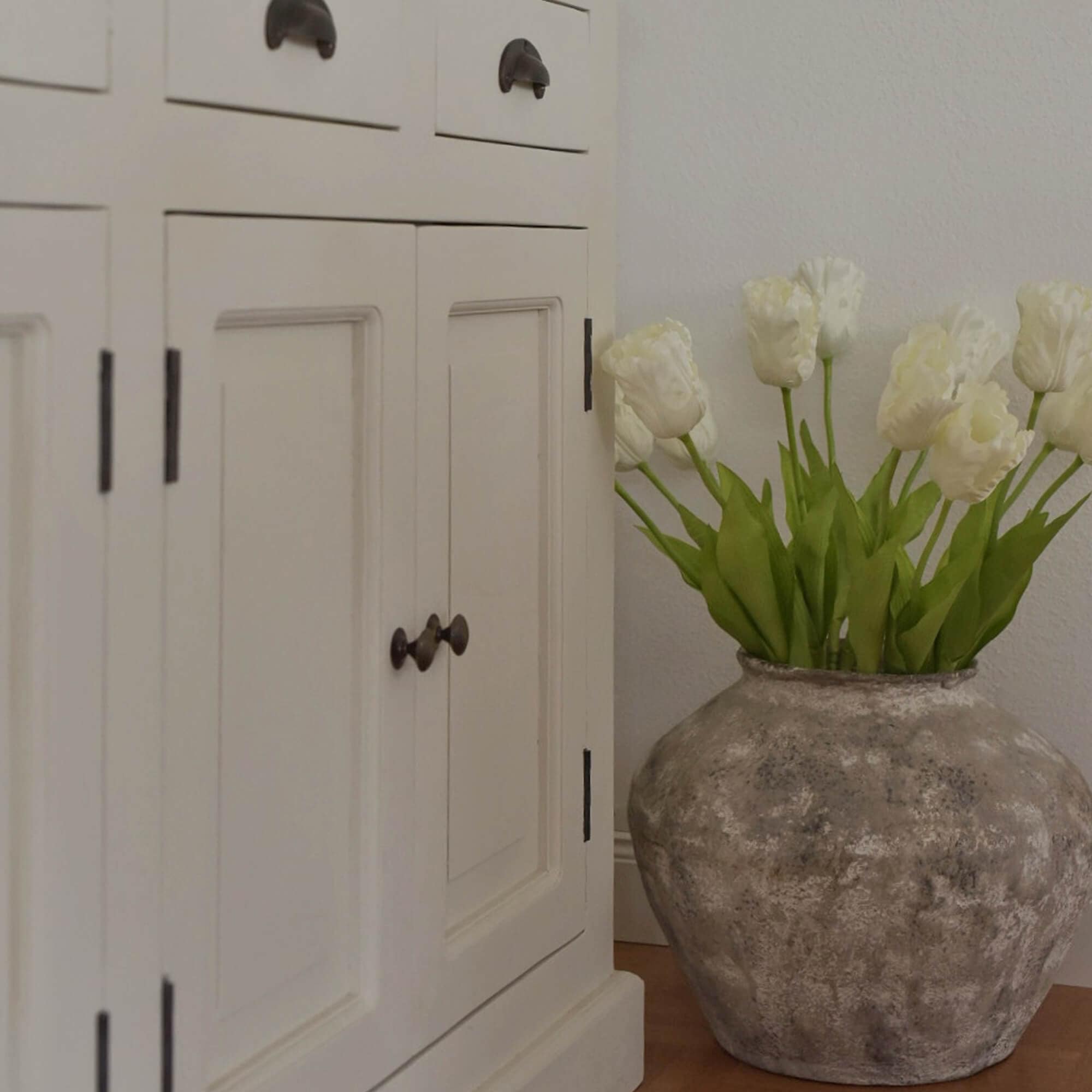Große graue Keramikvase mit weißen Tulpen neben weißem Holzschrank