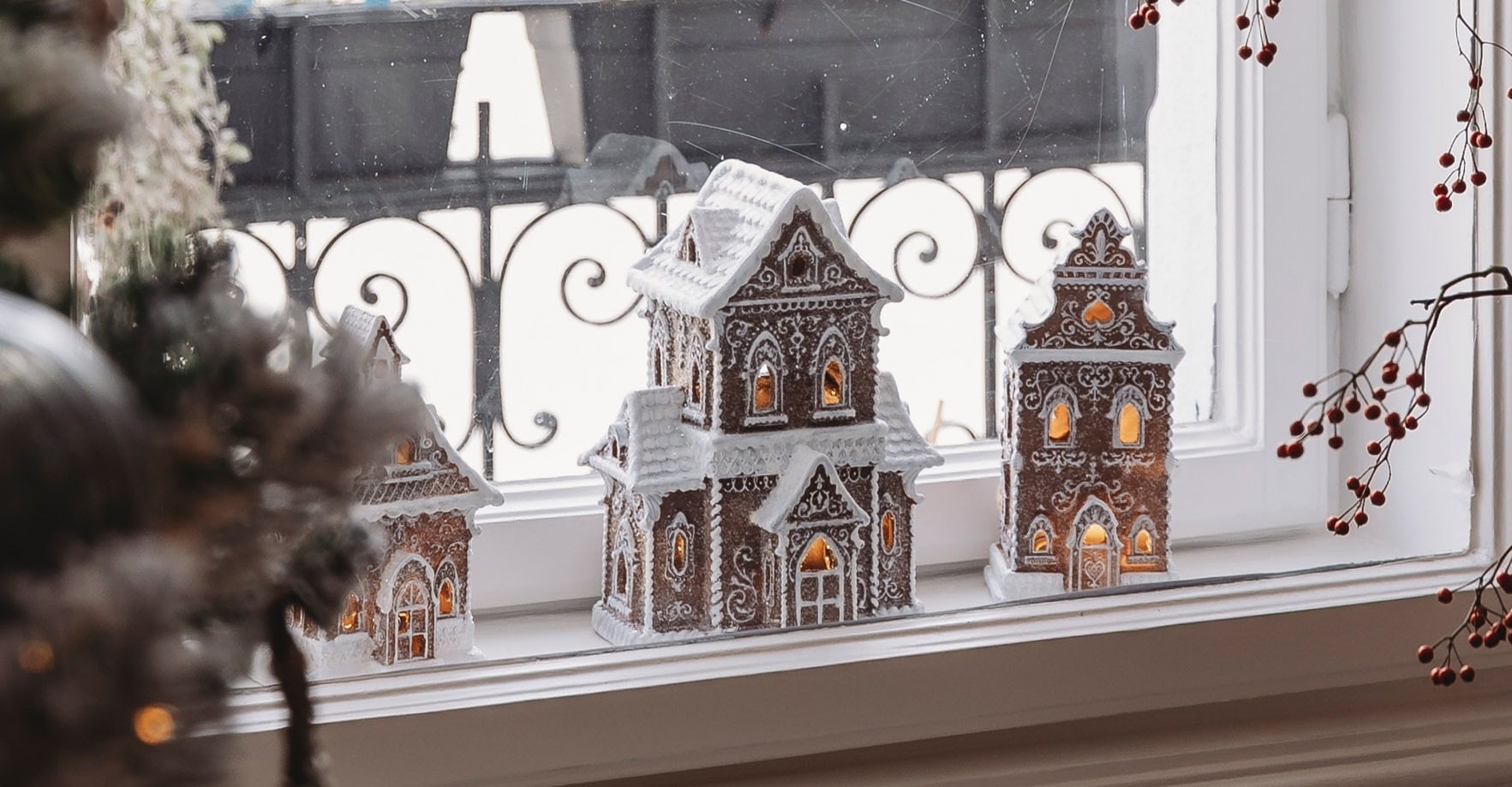 Dekorative Lebkuchenhäuser mit weißer Glasur und Beleuchtung auf dem Fensterbrett zur Weihnachtszeit