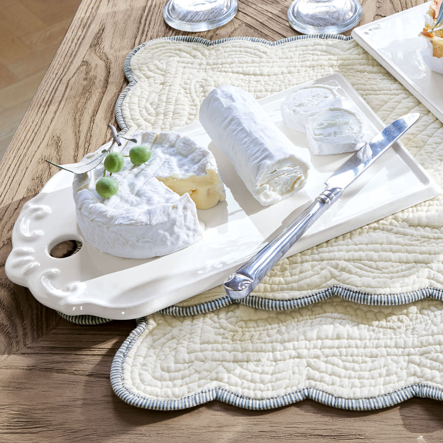 Keramikplatte mit weißem Ziegenkäse und Messer auf gesteppter cremefarbener Unterlage auf Holztisch