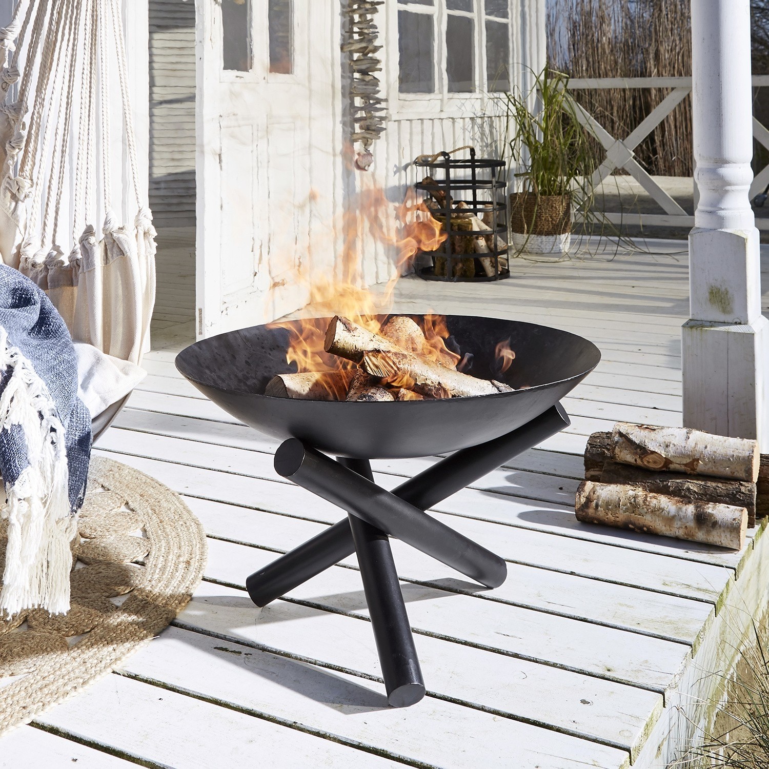 Schwarze Metall-Feuerschale mit Holz auf weißer Terrasse, moderner Garten-Grill