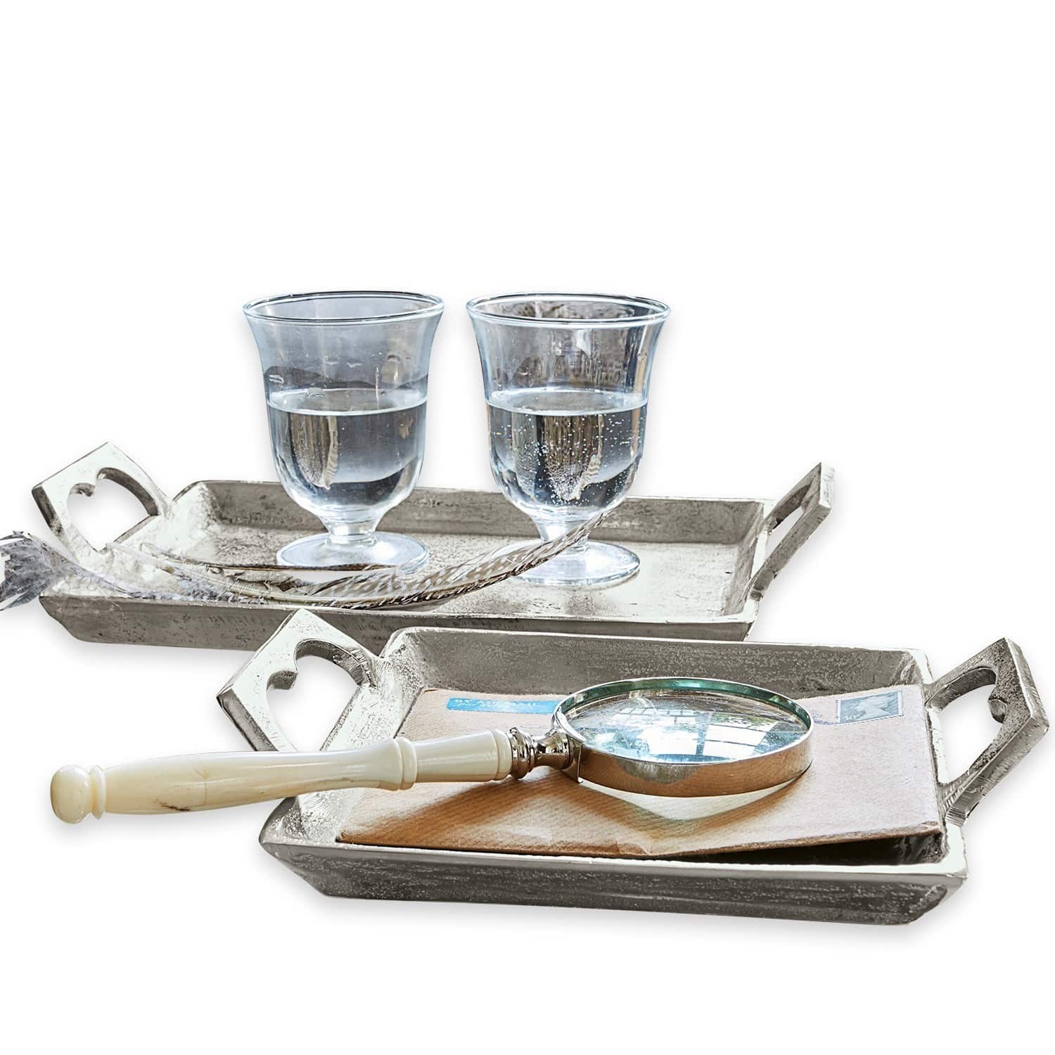Zwei silberne Metalltabletts mit Griffen, eines mit zwei Wassergläsern, das andere mit Lupe und Briefumschlag