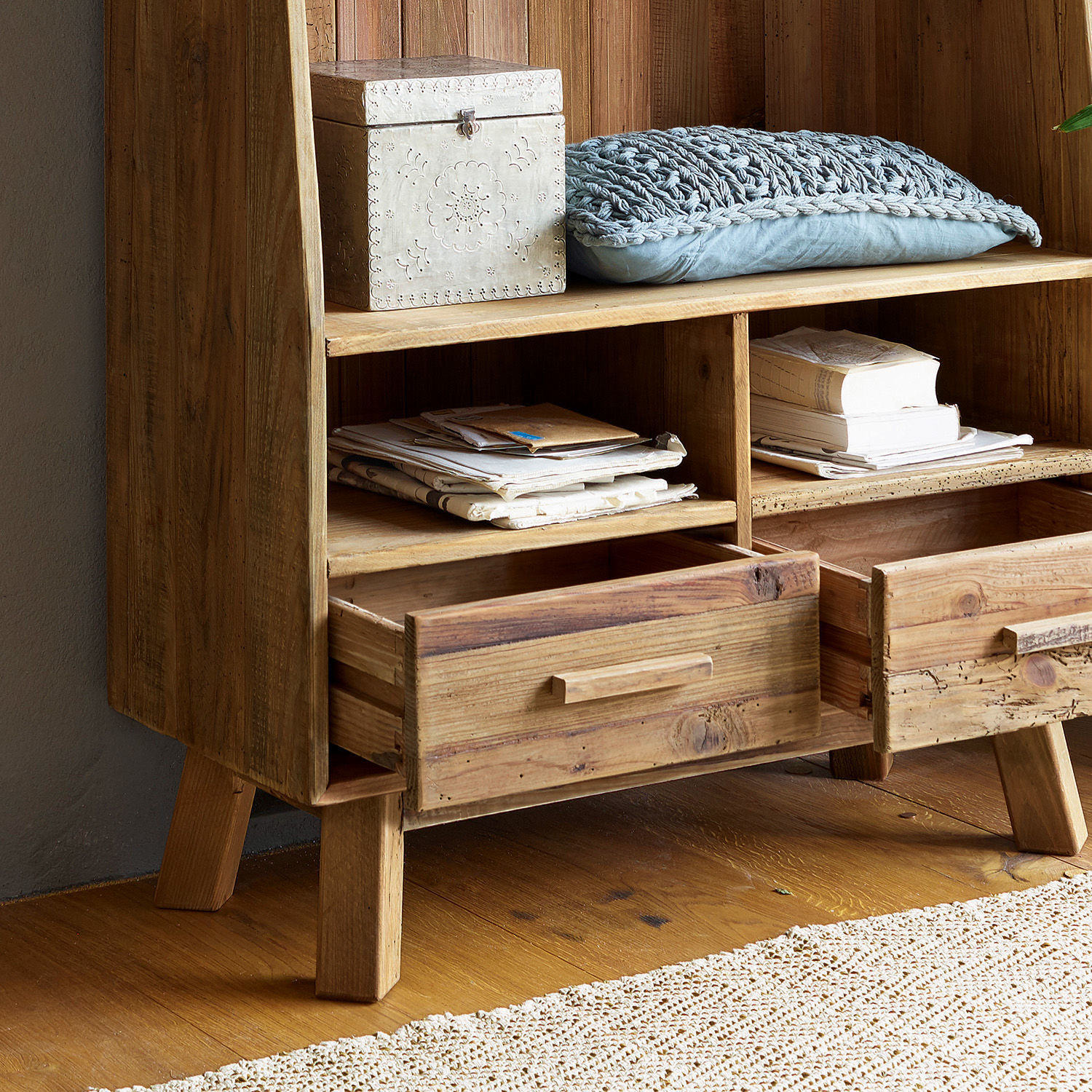 Holzschrank in Naturfarbe mit offenen Schubladen, grauem Zierkissen und dekorativer Box auf dem Regal