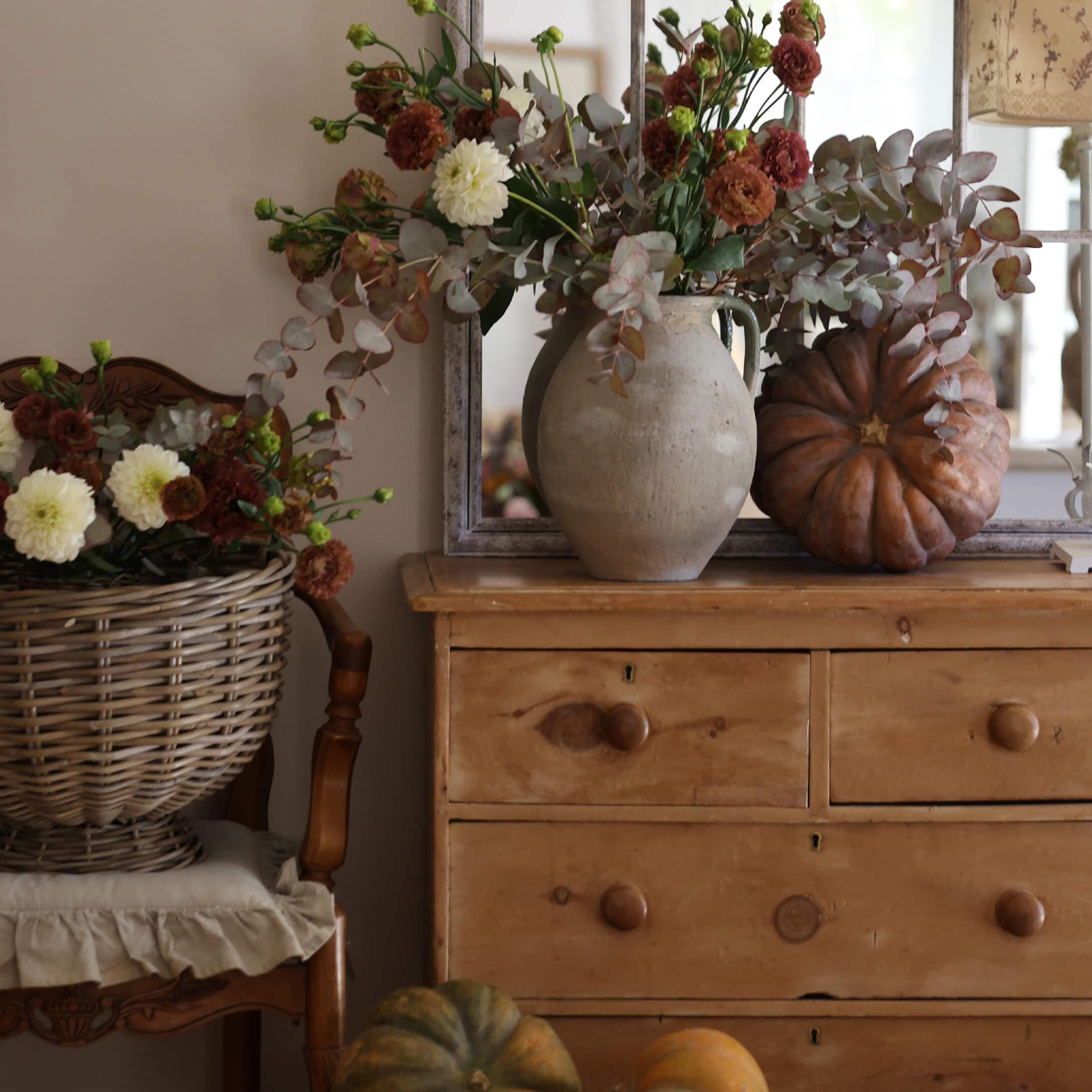 Rustikale Holzkommode mit Tonvase, herbstlichem Blumenstrauß und dekorativen Kürbissen in gemütlichem Raum
