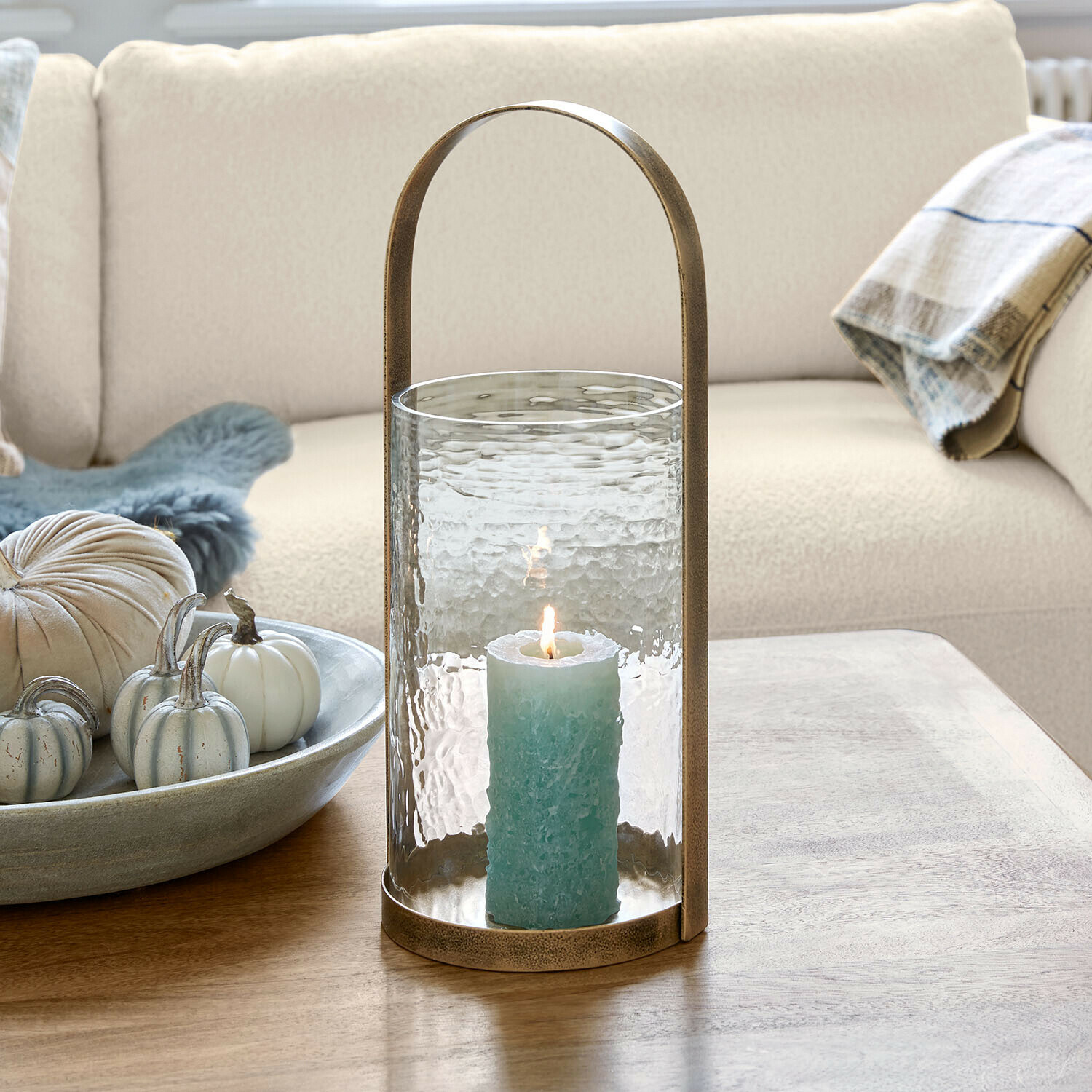 Windlicht Omirah Glaslaterne mit Messinggriff und blauer Kerze auf Holztisch im Wohnzimmer
