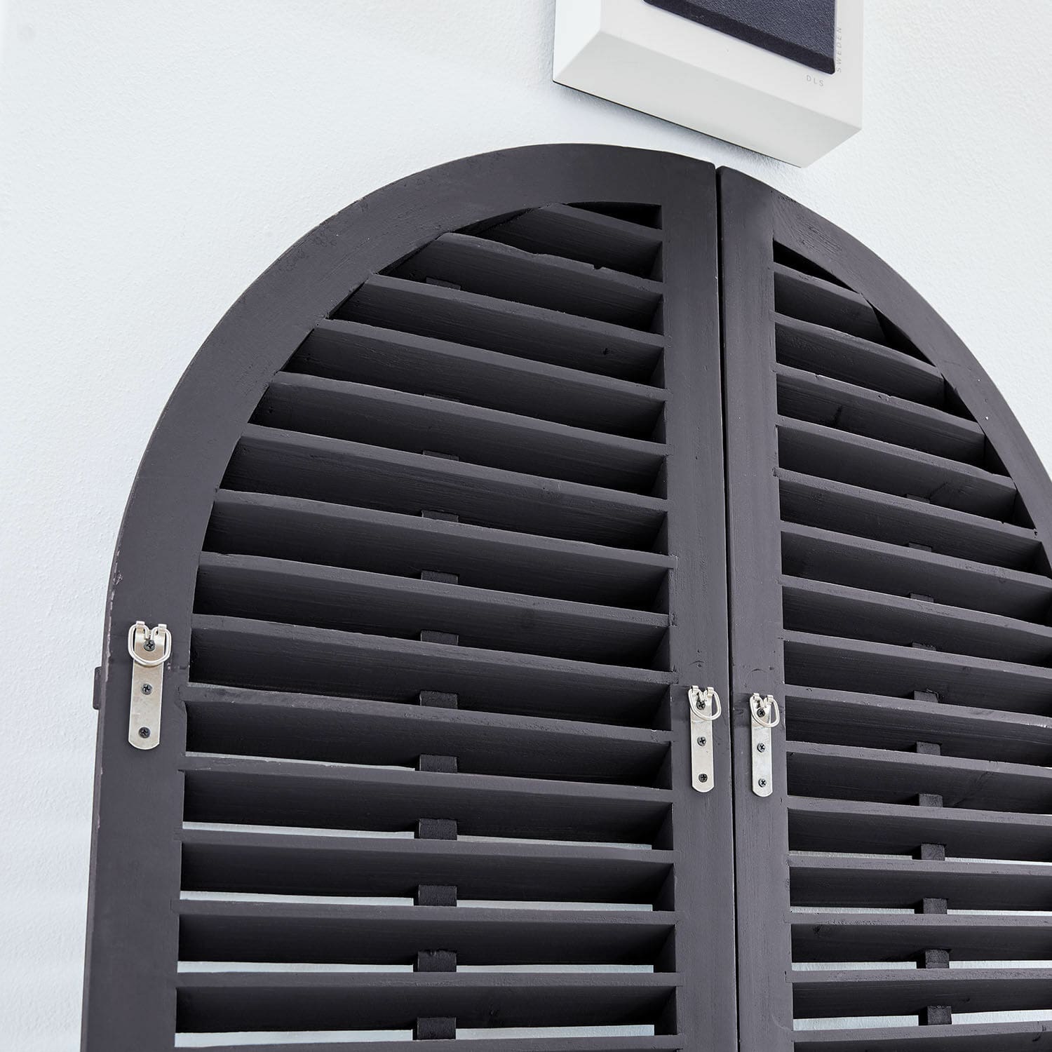 Schwarze halbkreisförmige Holzfensterläden mit Metallscharnieren an weißer Wand