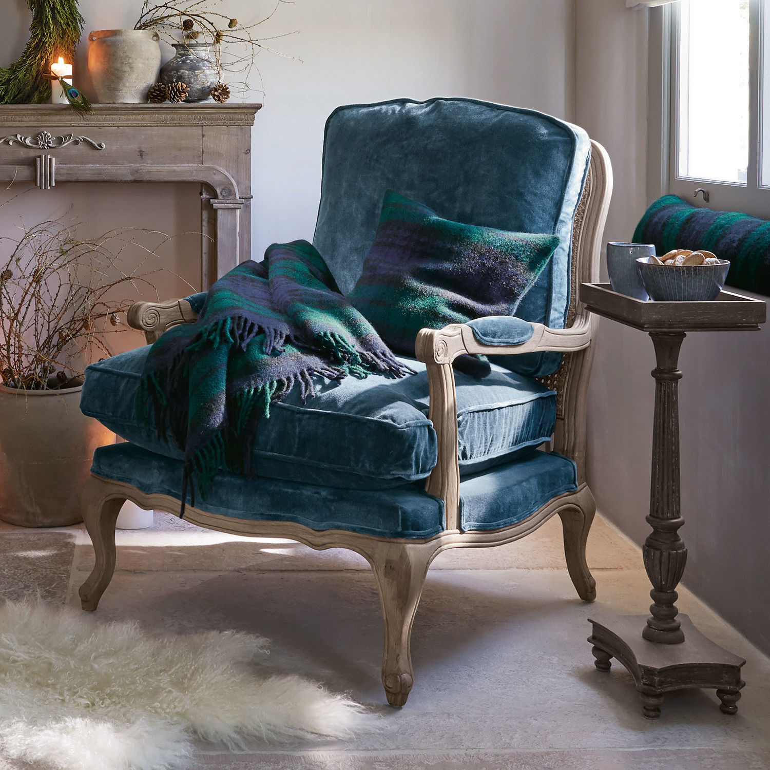 Blauer Samtfotel mit hellem Holzrahmen, grün-blauem Plaid und Kissen in gemütlichem Wohnzimmer
