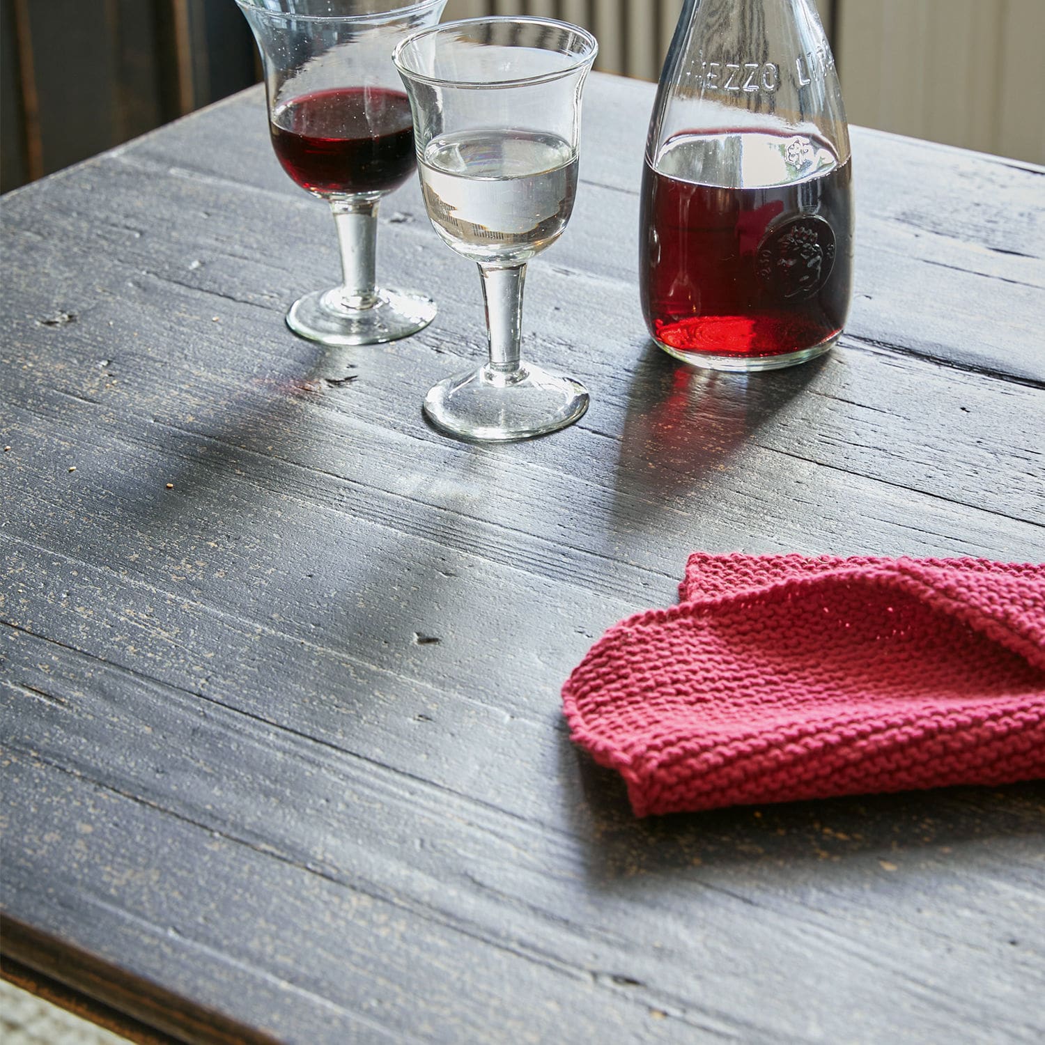 Gläser mit Rot- und Weißwein sowie Flasche auf Holztisch mit rotem Tuch