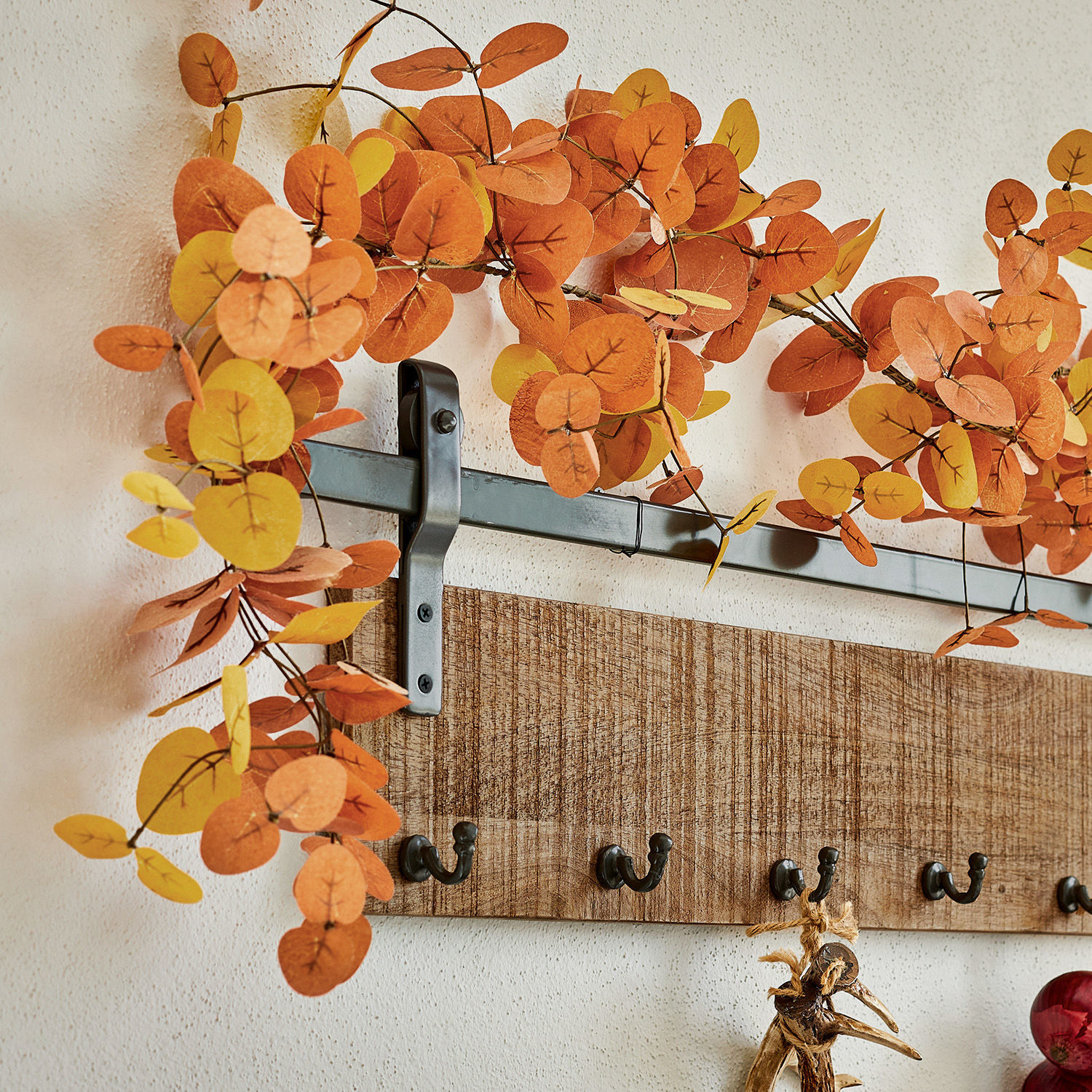 Wandgarderobe aus Holz mit Metallhaken und herbstlicher Dekoration aus orangefarbenen Blättern