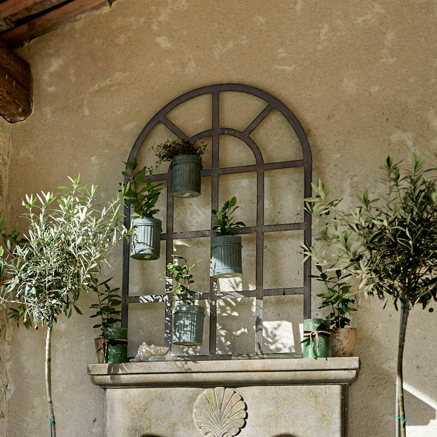 Metall-Wanddeko mit hängenden grünen Pflanztöpfen und Pflanzen vor beiger Wand