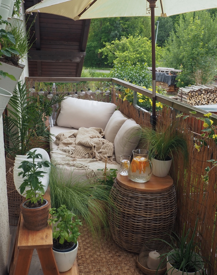 Gemütlicher Balkon mit beigem Sofa, Kissen, Rattantisch, Pflanzen und Sonnenschirm für Entspannung