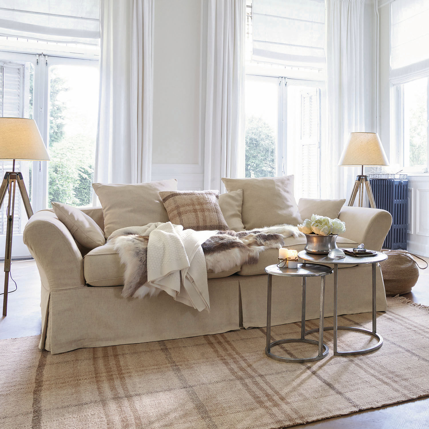 Sofa Worcester Beige Stoffsofa mit Kissen und Fell-Decke auf hellem Teppich in hellem Wohnzimmer mit Stehlampen