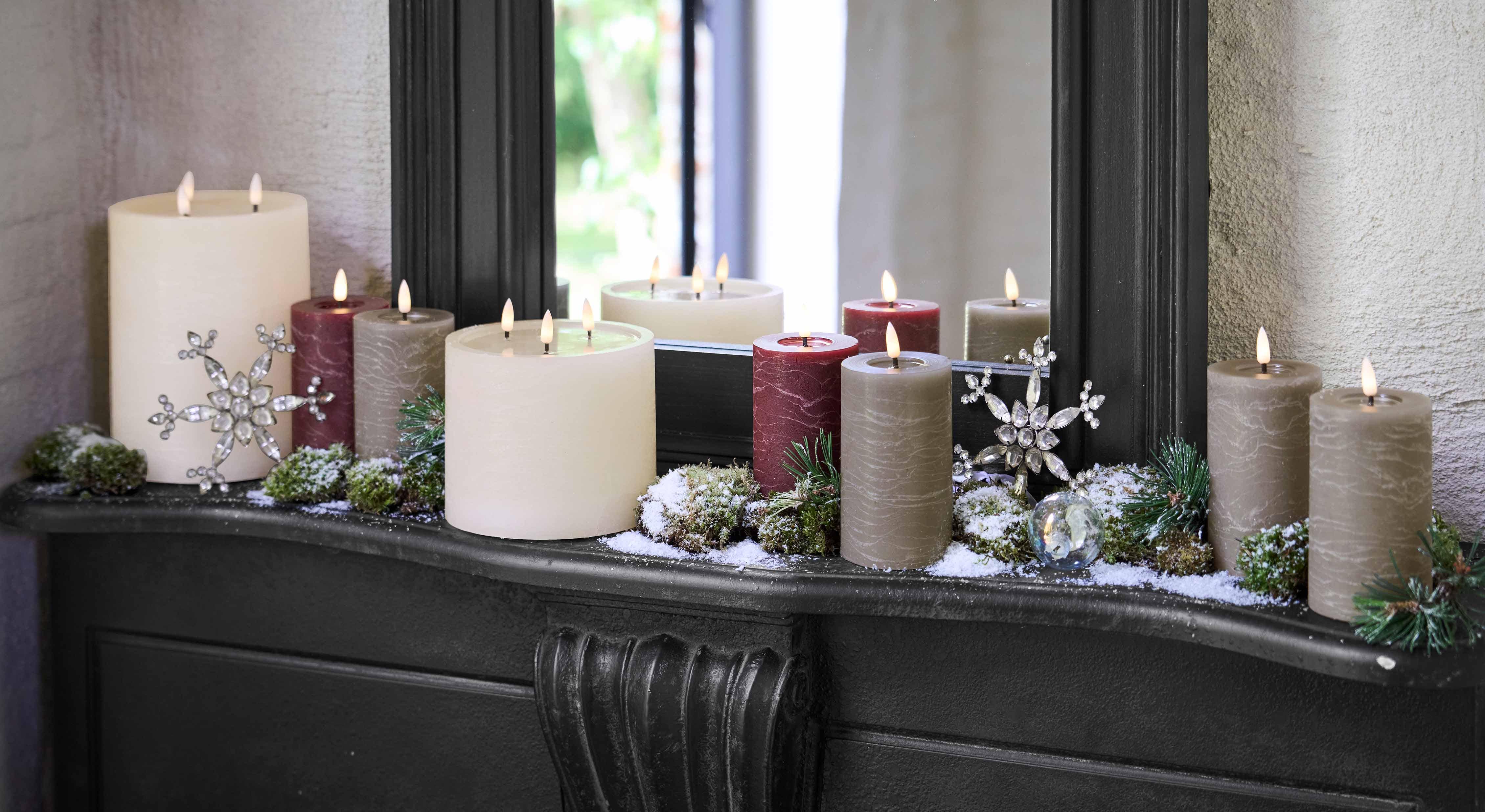 Dekoratives Kerzenset in Weiß, Bordeaux und Grau auf Kamin mit winterlichen Accessoires