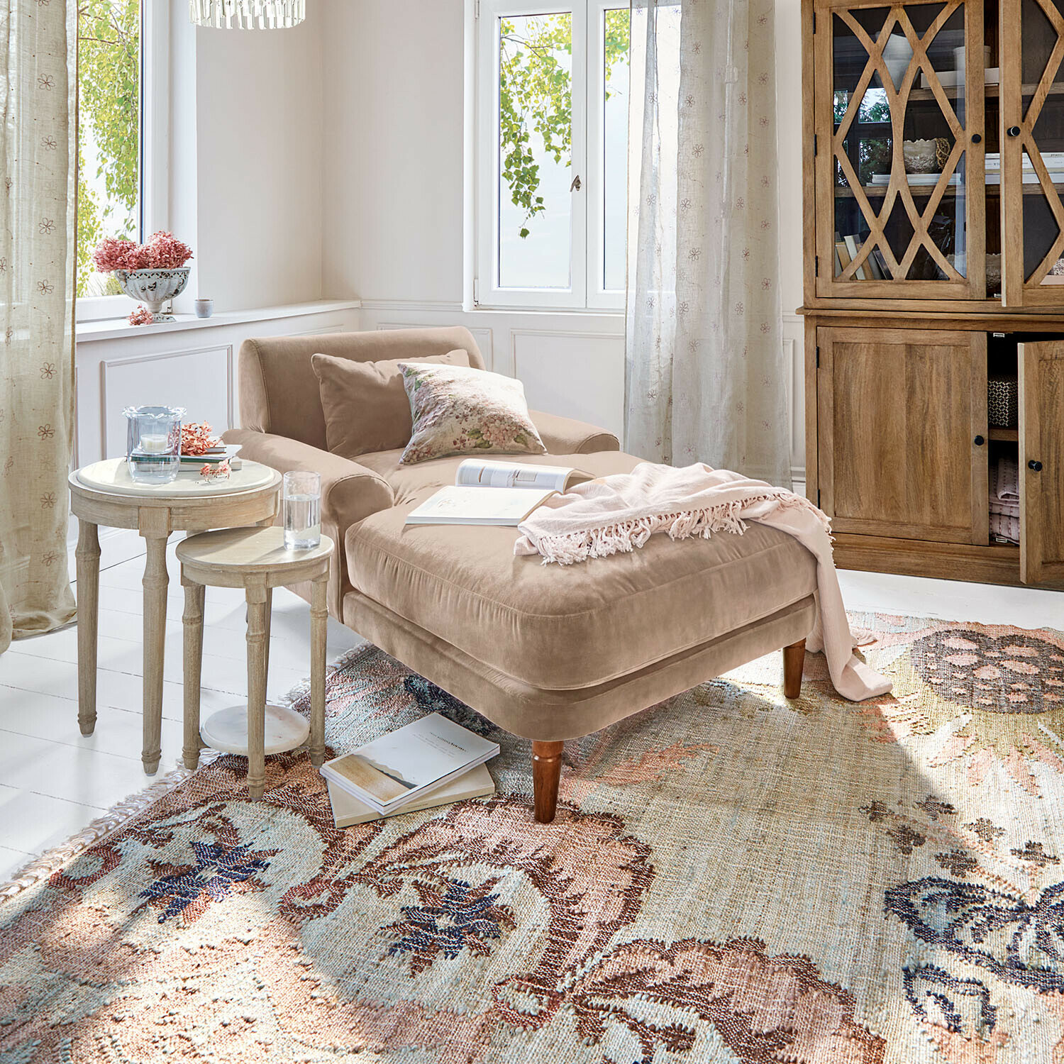 Beige Samt-Chaiselongue mit Kissen und rosa Decke auf gemustertem Teppich in hellem Wohnzimmer