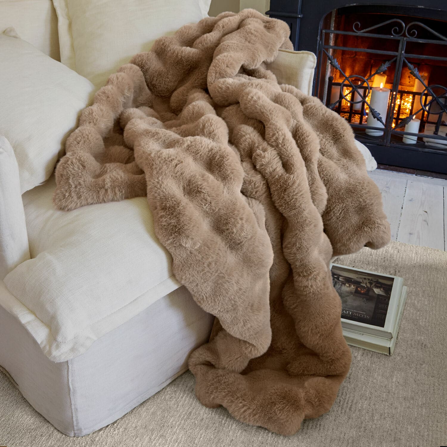 Plaid Zalina Weiche beige Kunstfell-Decke auf hellem Sofa vor Kamin für gemütliche Wohnatmosphäre