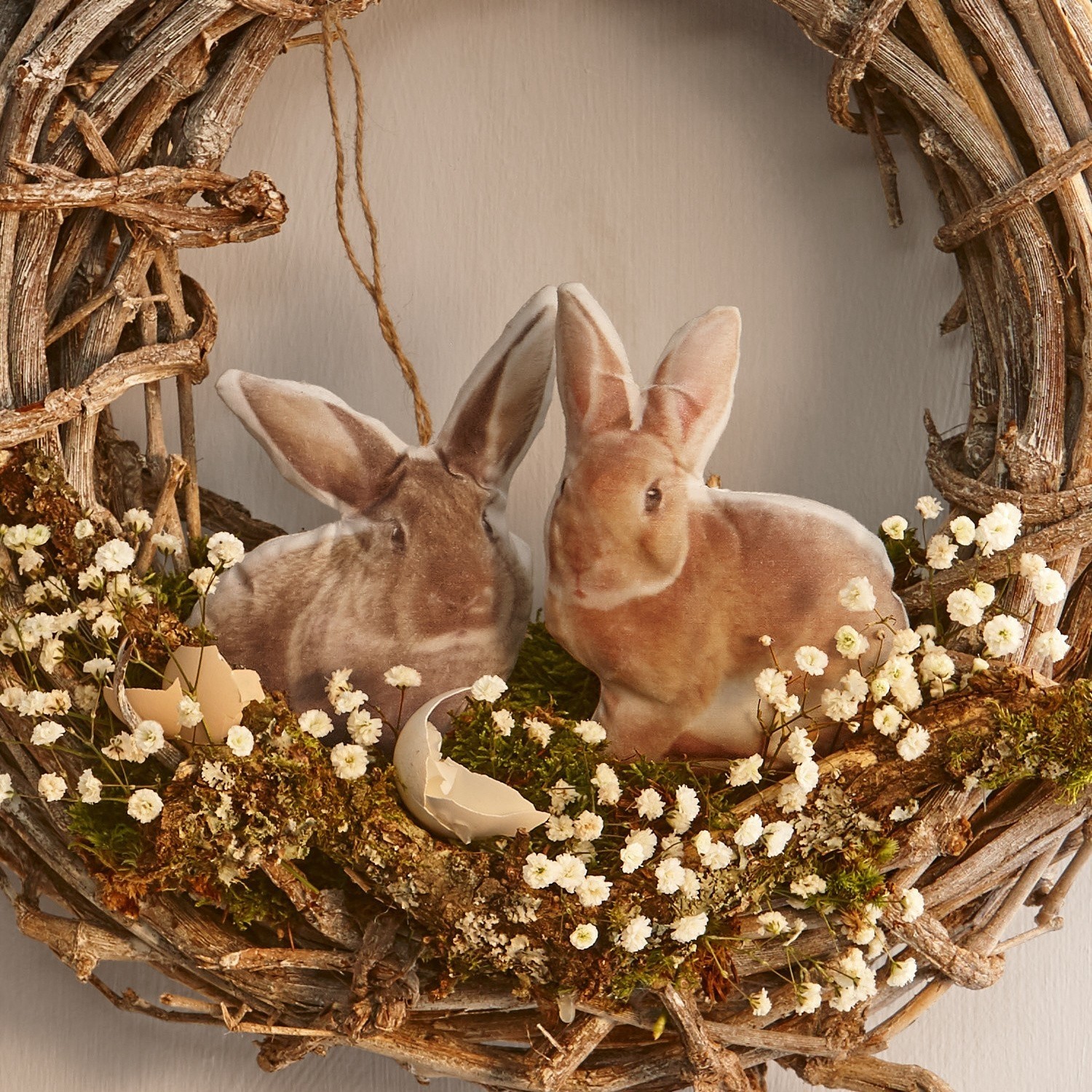 Kranz aus Zweigen mit zwei Plüschhasen und weißen Blüten als Osterdekoration