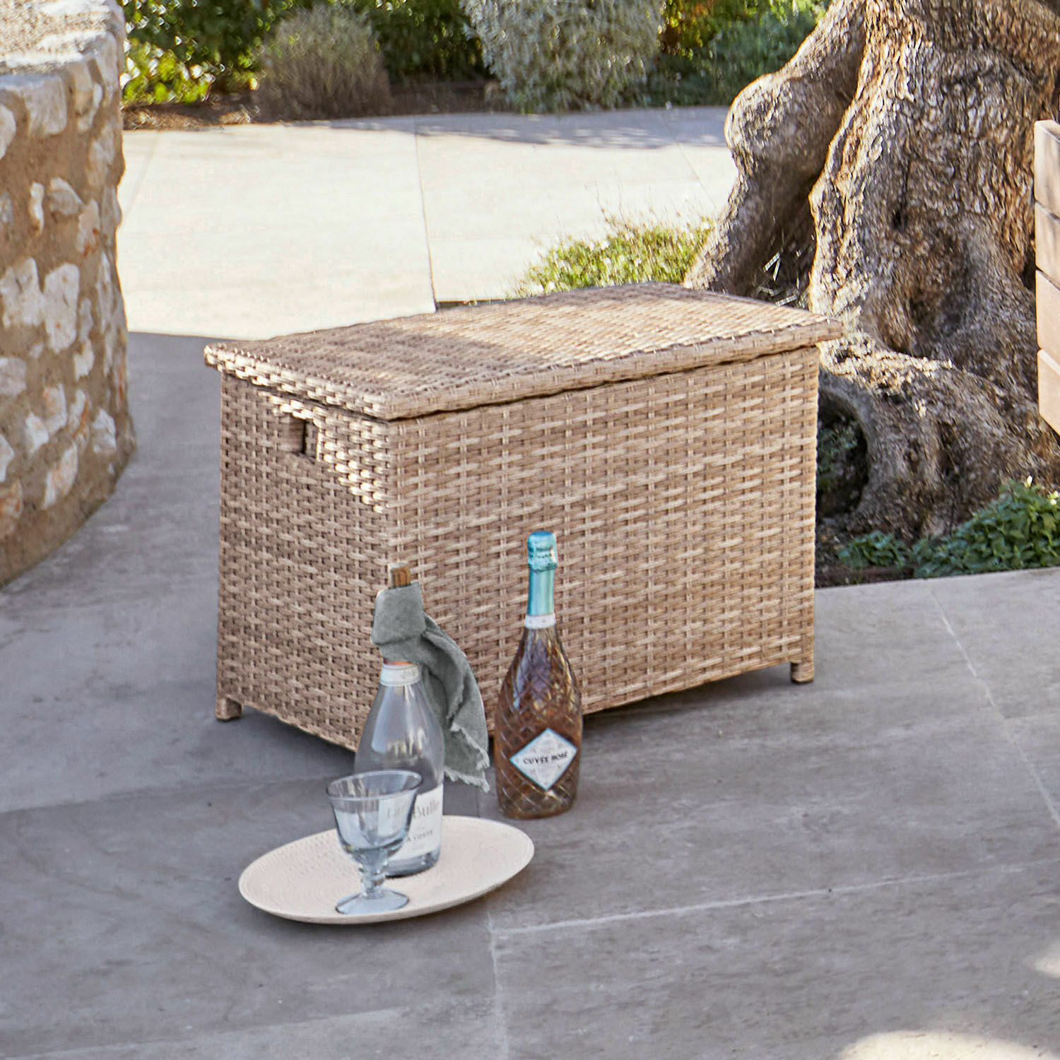 Rattankiste in Naturfarbe auf Terrasse mit Flaschen und Glas auf Boden