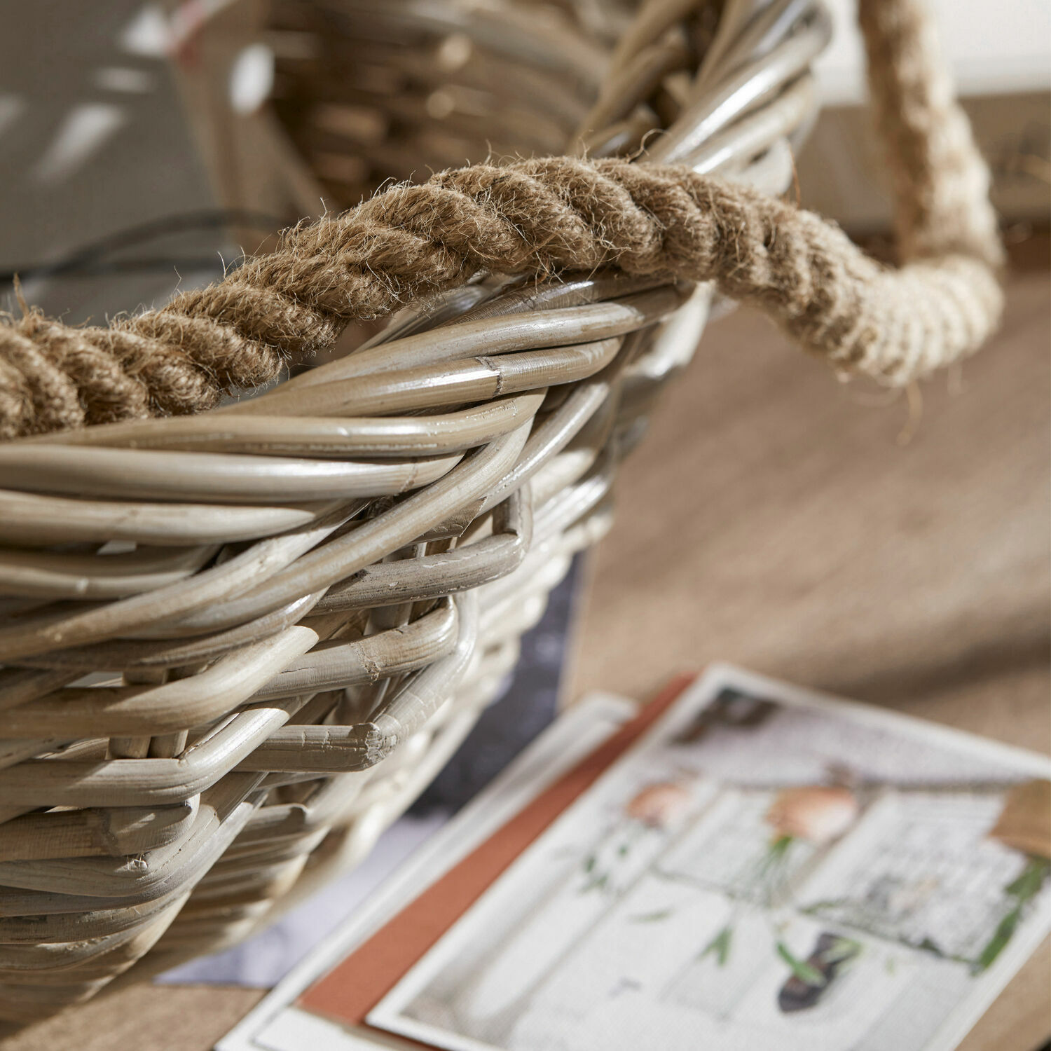 Natürlicher beiger Rattankorb mit Hanfgriff auf Holztisch mit Zeitschriften