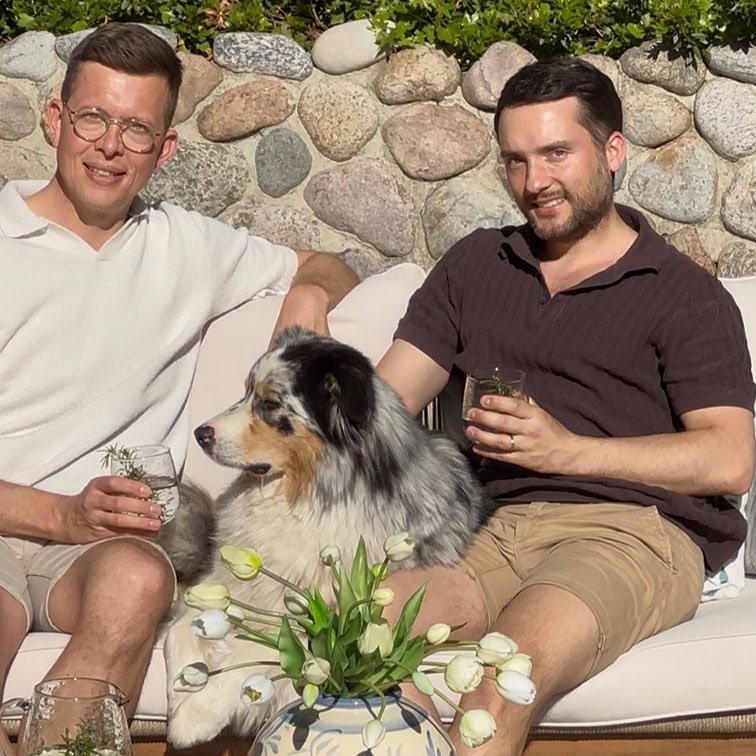 Zwei Männer sitzen draußen auf einer Couch mit einem Australian Shepherd und weißen Tulpen im Vordergrund.