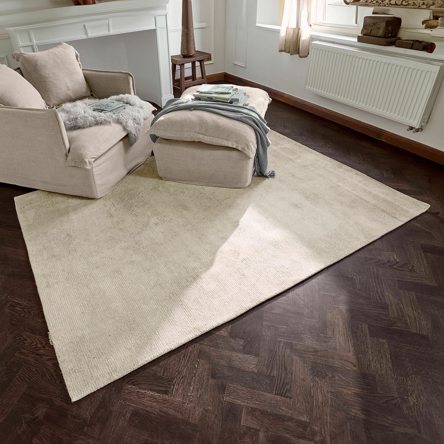 Teppich Zaniyah Beiger Teppich aus weichem Material auf dunklem Holzboden in hellem Wohnzimmer mit Sessel