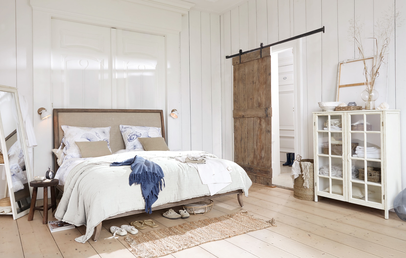 Helle Schlafzimmer mit Holzbett, weißer Bettwäsche und rustikalem Glas-Holz-Schrank
