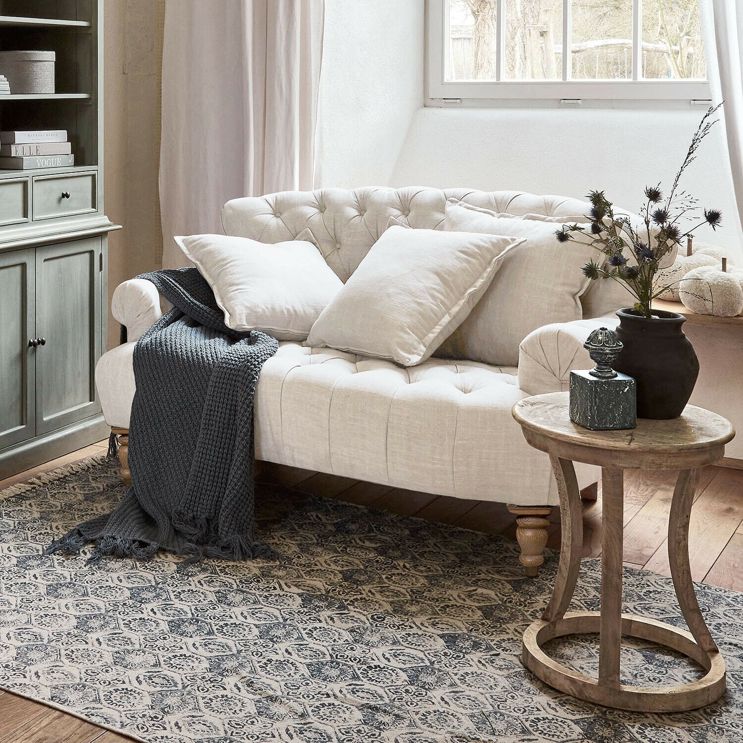 Beiges, gesteppte Leinen-Sofa mit Kissen und grauer Strickdecke in gemütlichem Wohnzimmer mit Holztisch