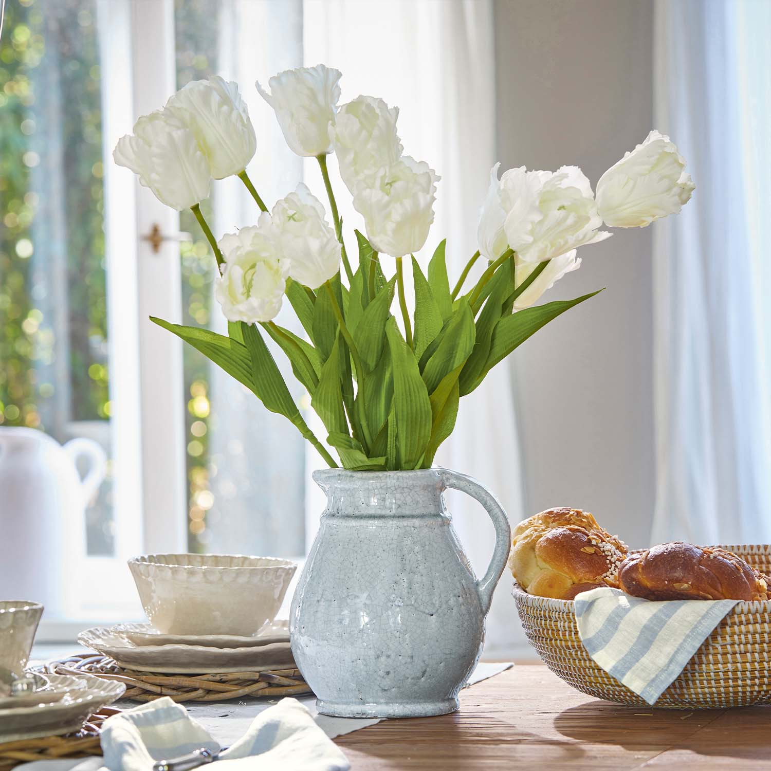 Weißer Keramikkrug mit grünen künstlichen Tulpen auf Holztisch mit Gebäck