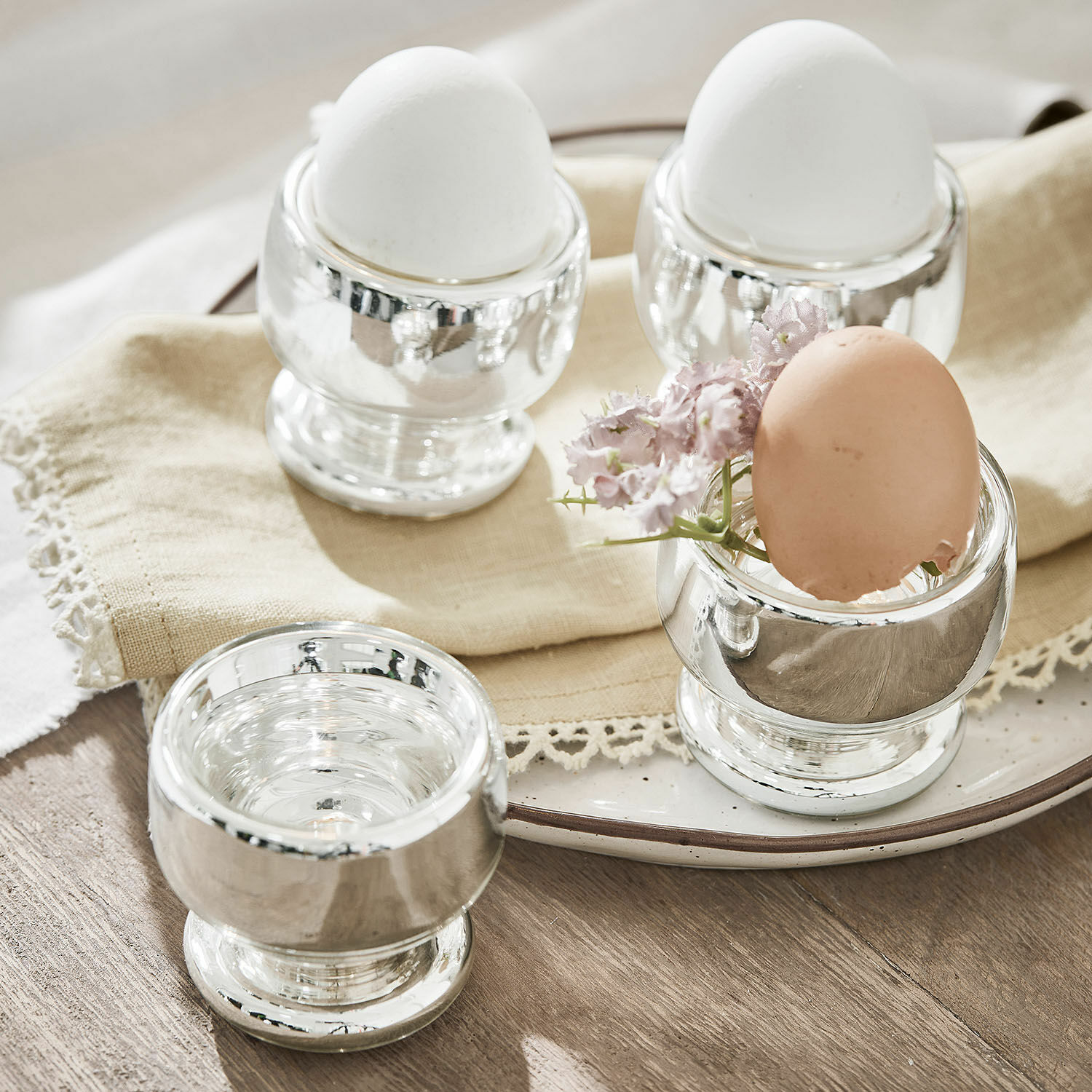 Set aus silbernen Metall-Eierbechern mit weißen und braunen Eiern auf hellem Holztisch