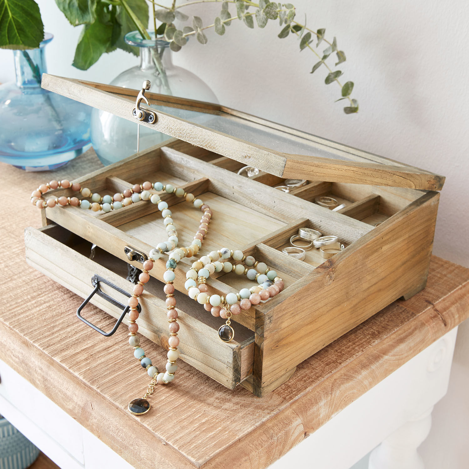 Holz-Schmuckkasten mit Glasdeckel und Fächern, dekoriert mit bunten Perlenketten und Ringen