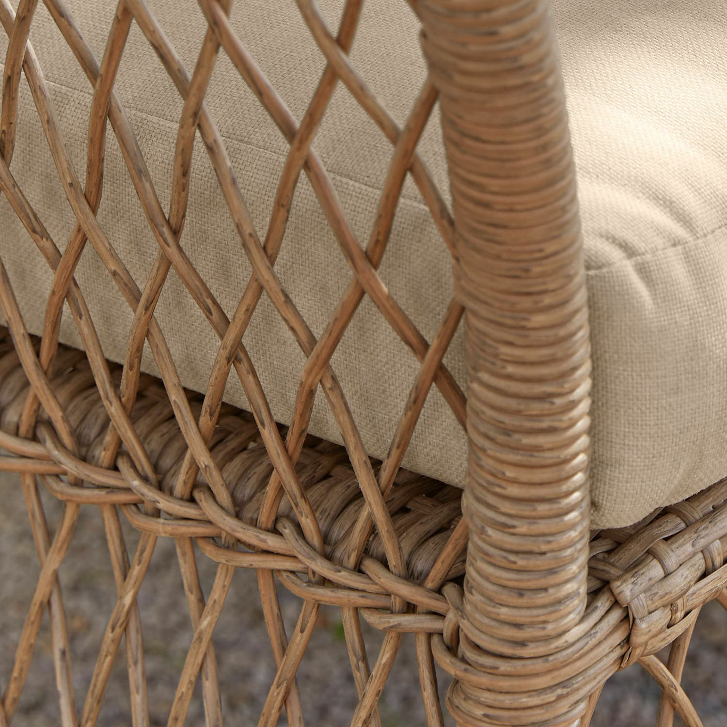 Nahaufnahme eines Rattanstuhls mit beigem Stoffkissen, Gartenmöbel aus natürlichem Rattan