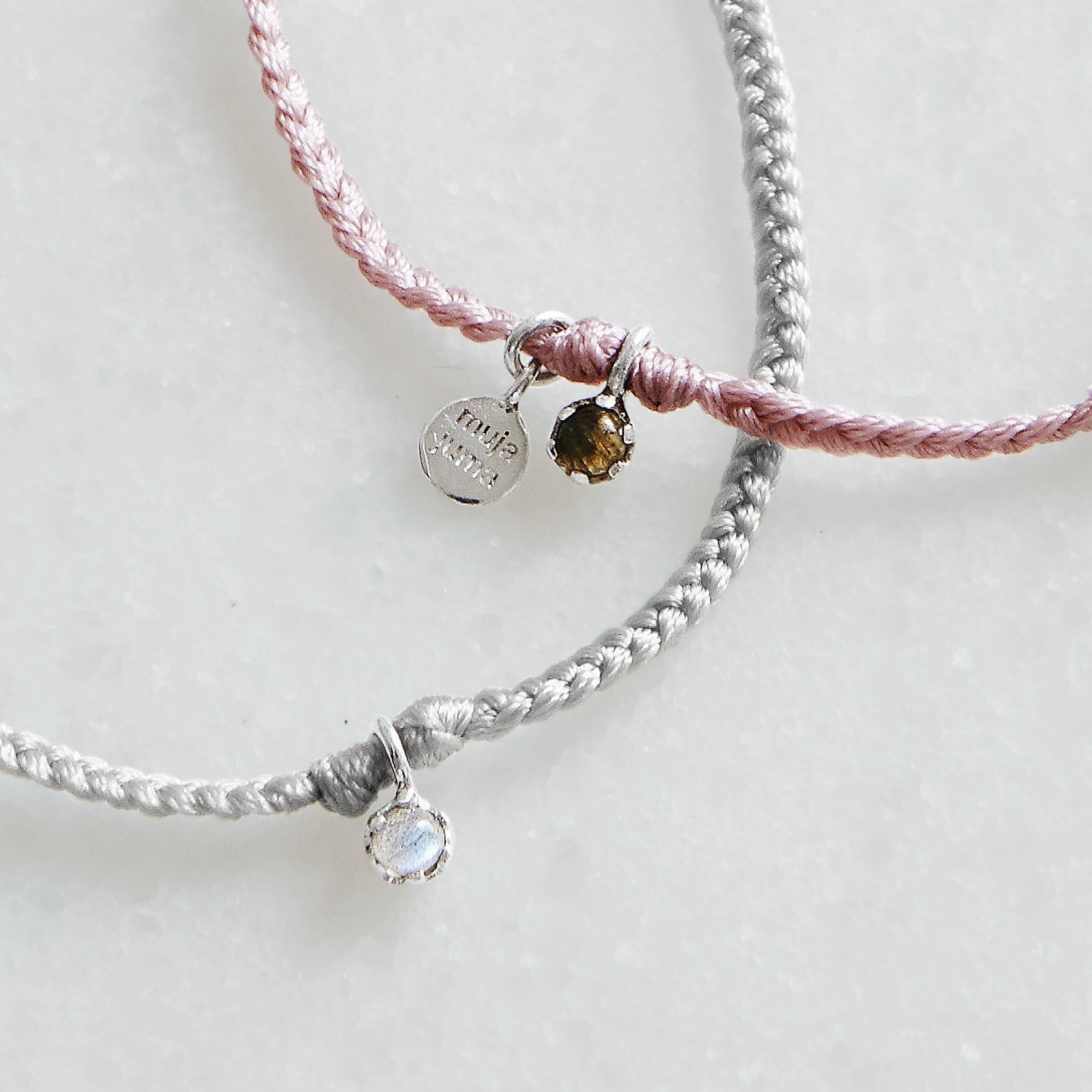 Feine Armbänder aus geflochtenem rosa und grauem Garn mit kleinen Edelsteinanhängern