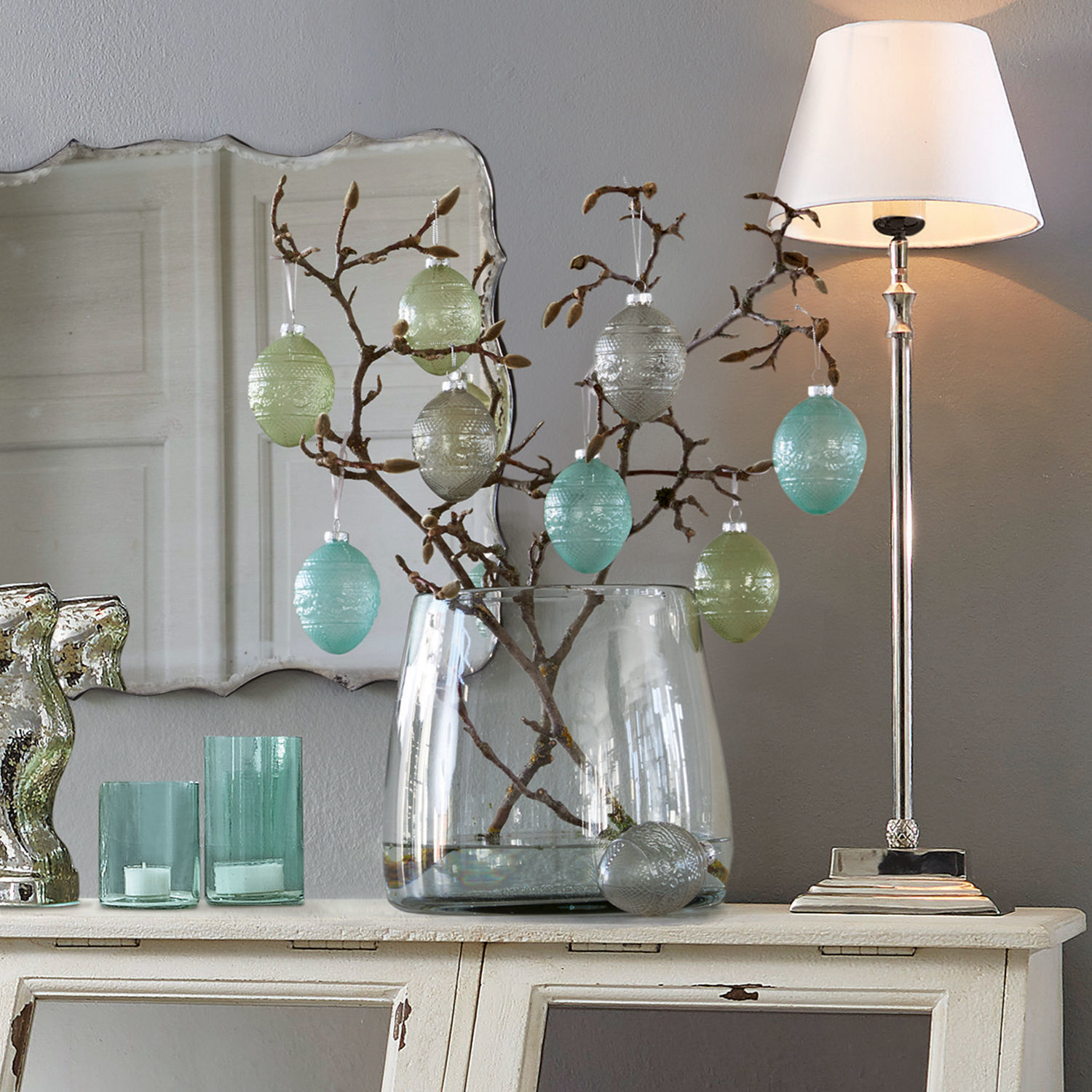 Vase Inga Dekorative Glas-Eier in Pastellfarben an Zweigen in klarem Glasvase auf weißem Sideboard