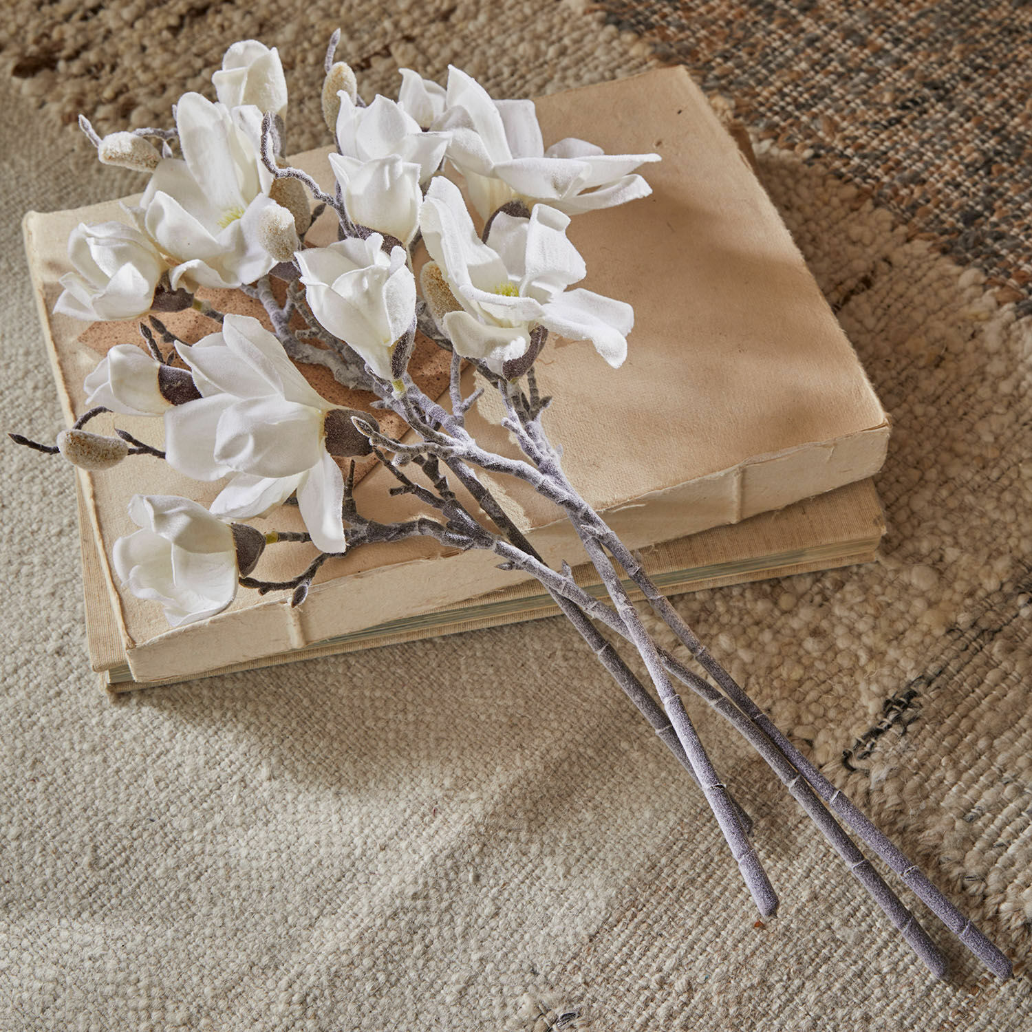 Deko-Blume 4er Set Santavella Strauß weiße Magnolienblüten aus Stoff auf beigen Büchern auf strukturiertem Teppich