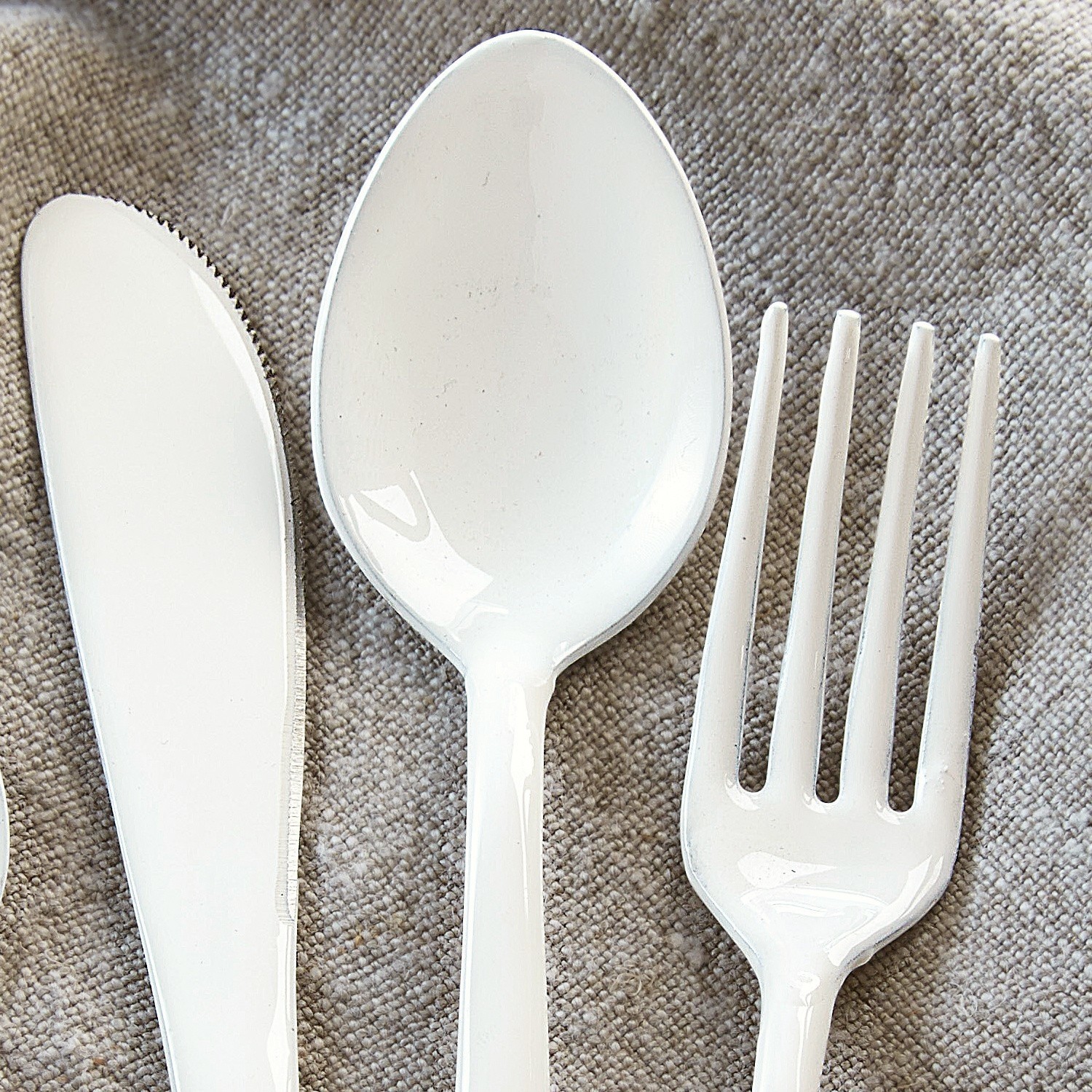 Weißes Plastikmesser, Löffel und Gabel auf grauem Stoff, praktisches Besteck für den Alltag