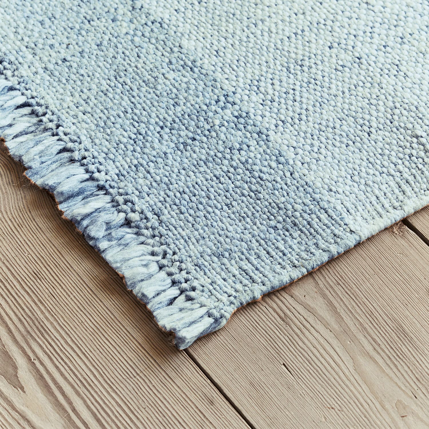 Blauer Wollteppich mit Fransen auf Holzboden, weich und dekorativ