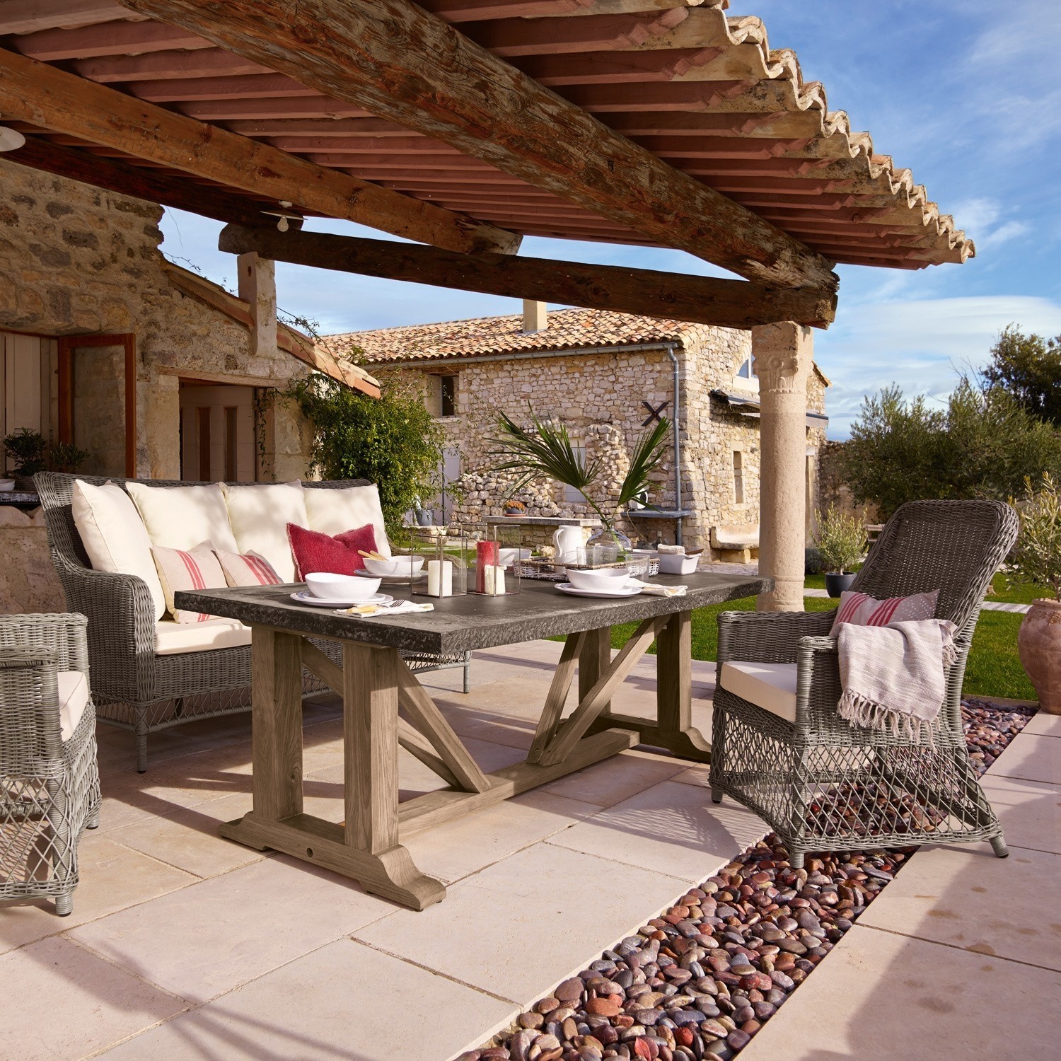 Gartenmöbel-Set aus grauem Rattan mit Holztisch auf Terrasse vor steinernem Haus
