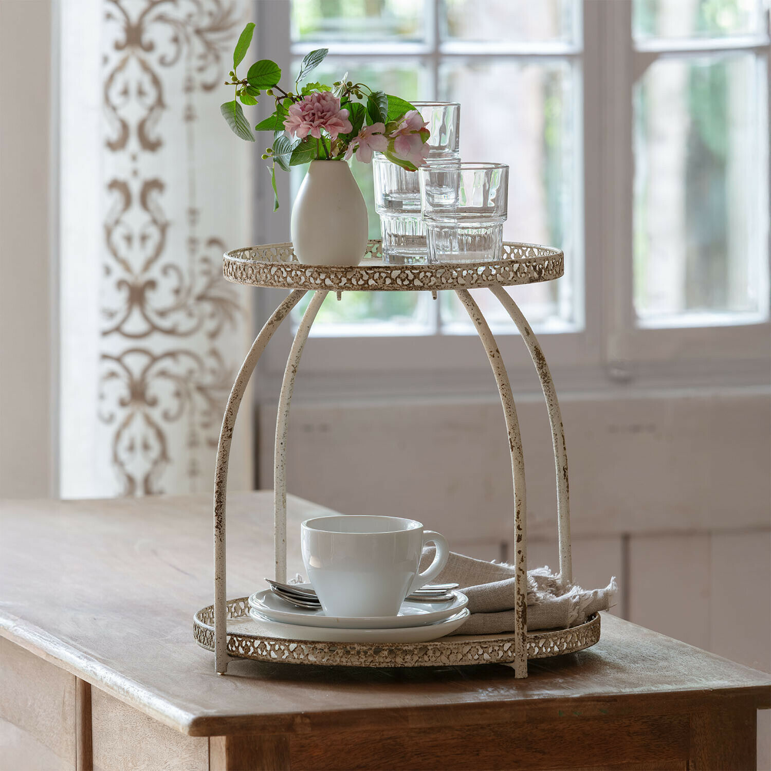 Etagere Nolienne Zweistöckiger Metallständer im Vintage-Stil in Creme mit Tasse und Gläsern auf Holztisch