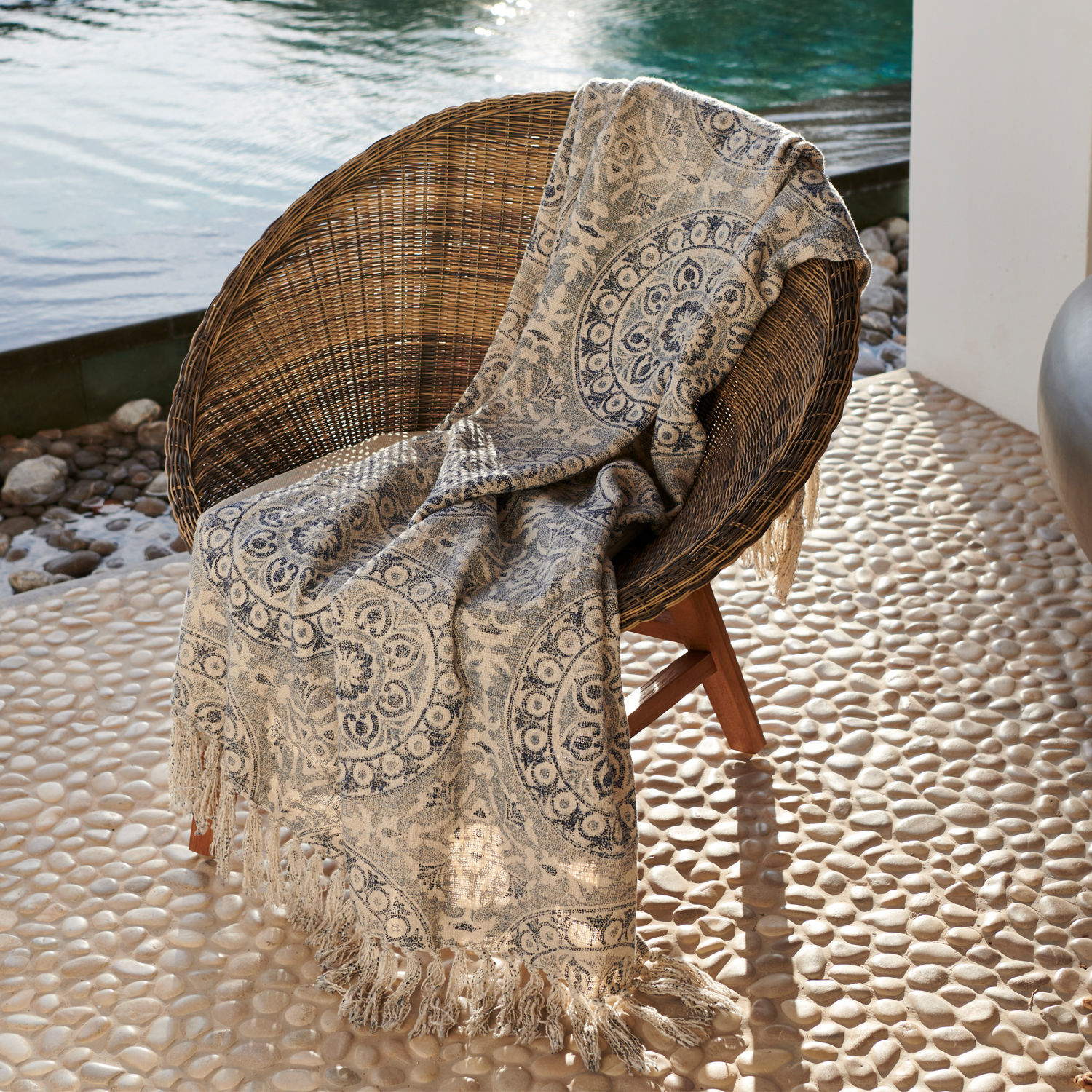Beige Decke mit blauem Muster und Fransen auf Rattanstuhl auf Terrasse am Wasser