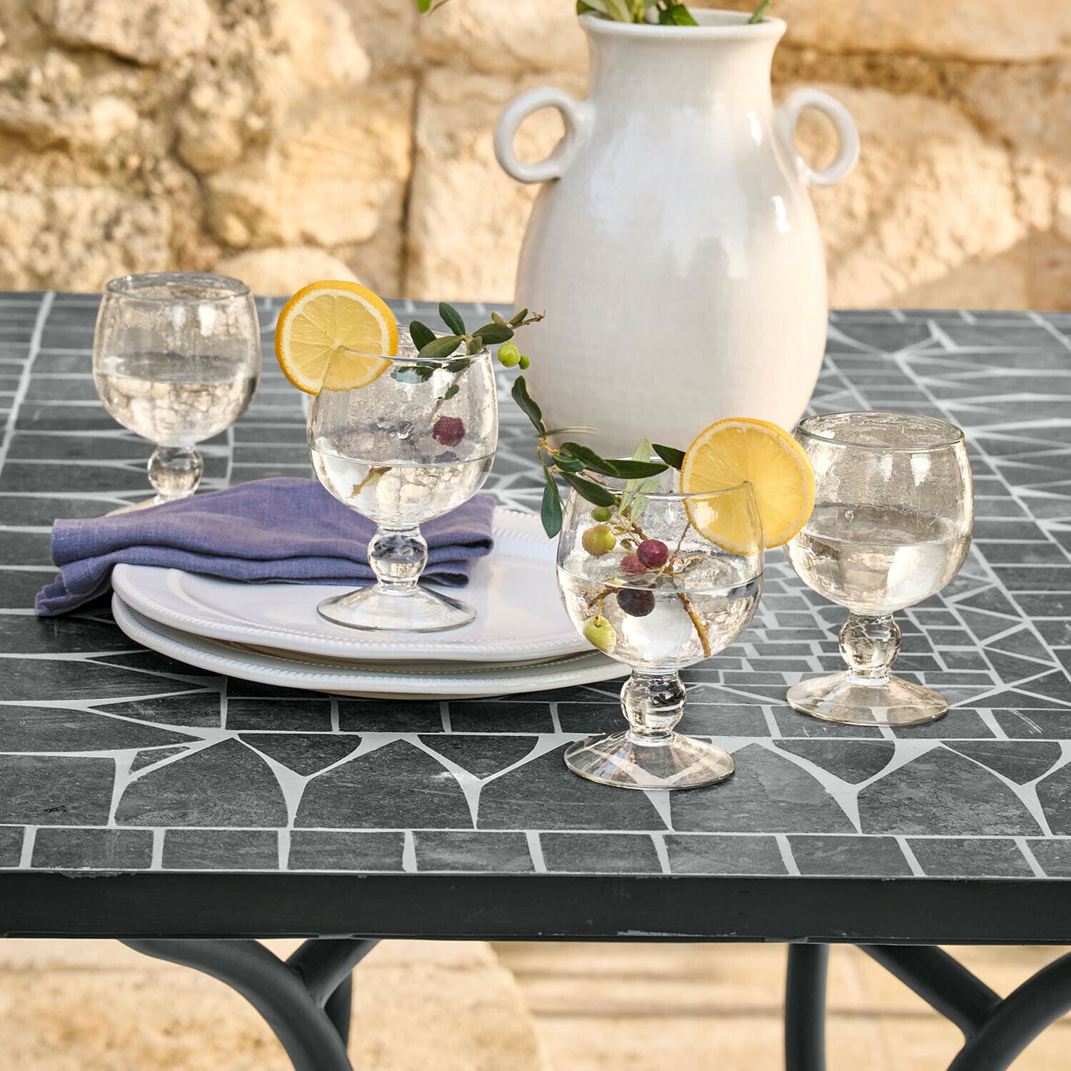 Glas 4er Set Vinoros Gläser mit Wasser und Zitronenscheiben auf schwarzem Mosaiktisch, weiße Keramikvase im Hintergrund