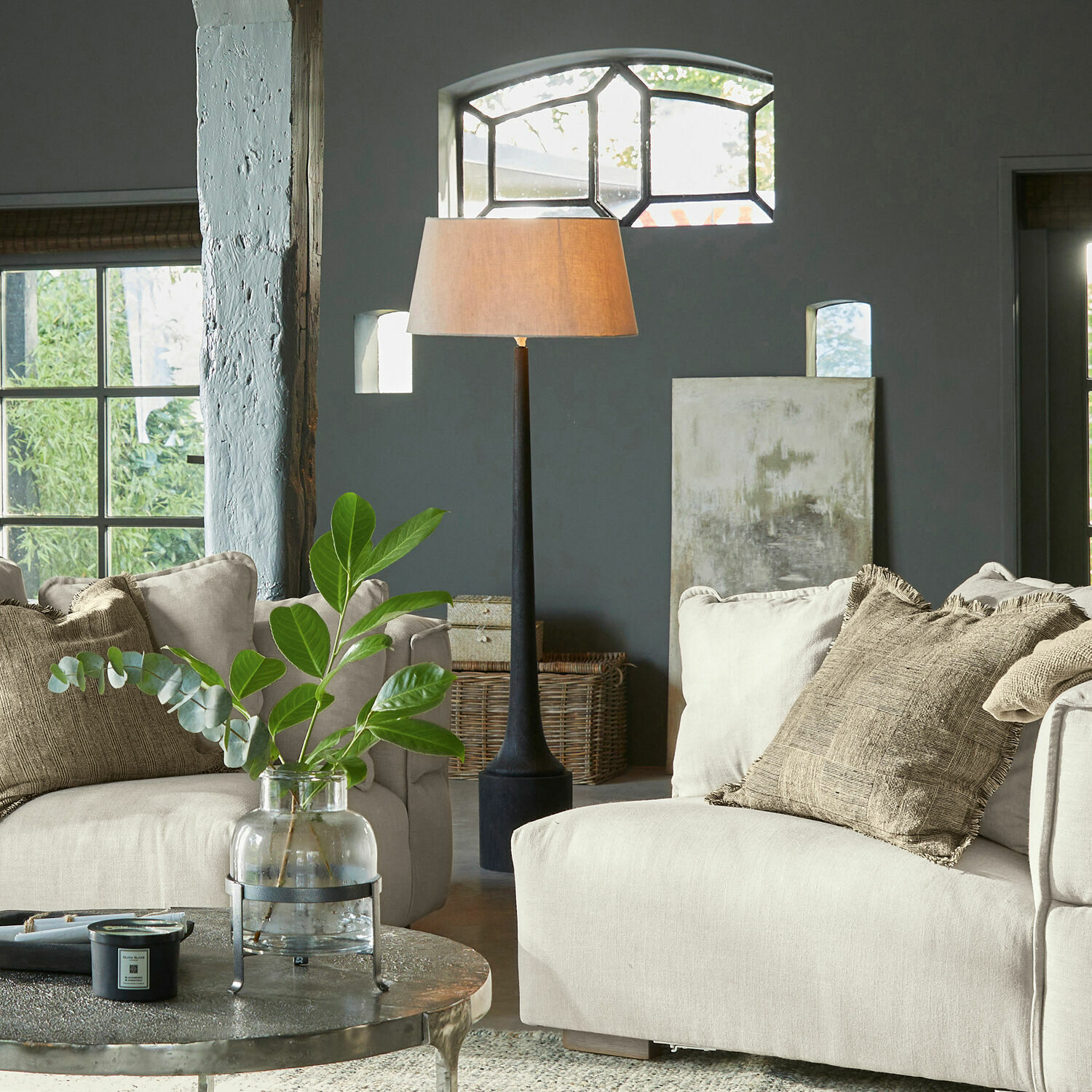 Gemütliches Wohnzimmer mit beigem Stoffsofa und Stehlampe mit schwarzem Sockel, Pflanzen-Deko